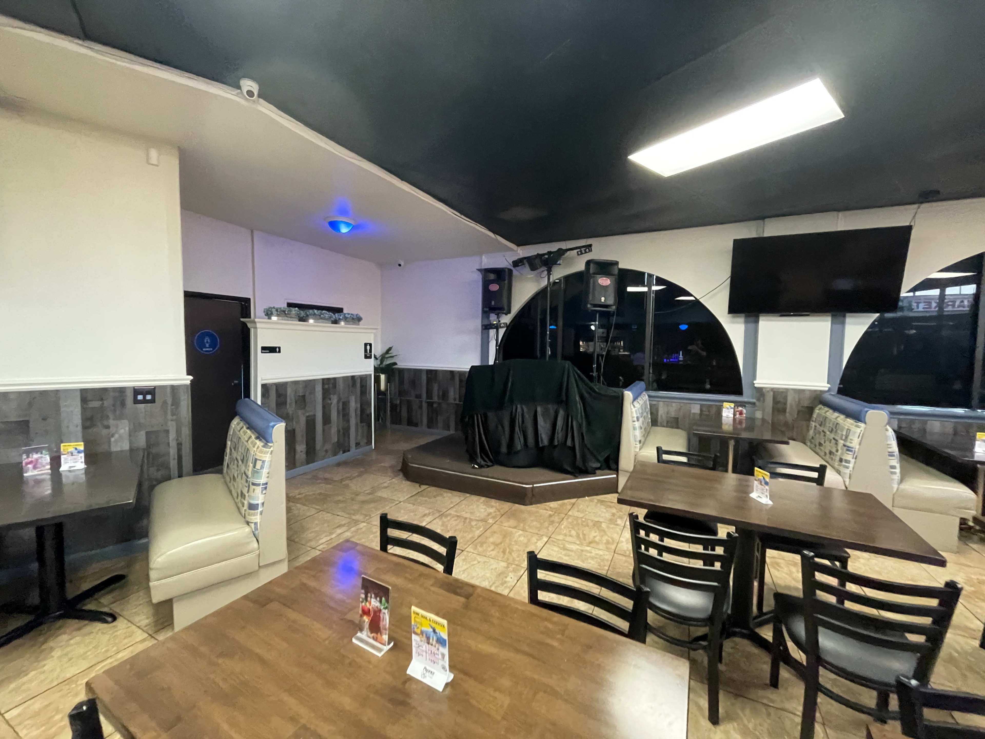 An empty restaurant interior with tables, chairs, and a stage area covered by a black cloth.