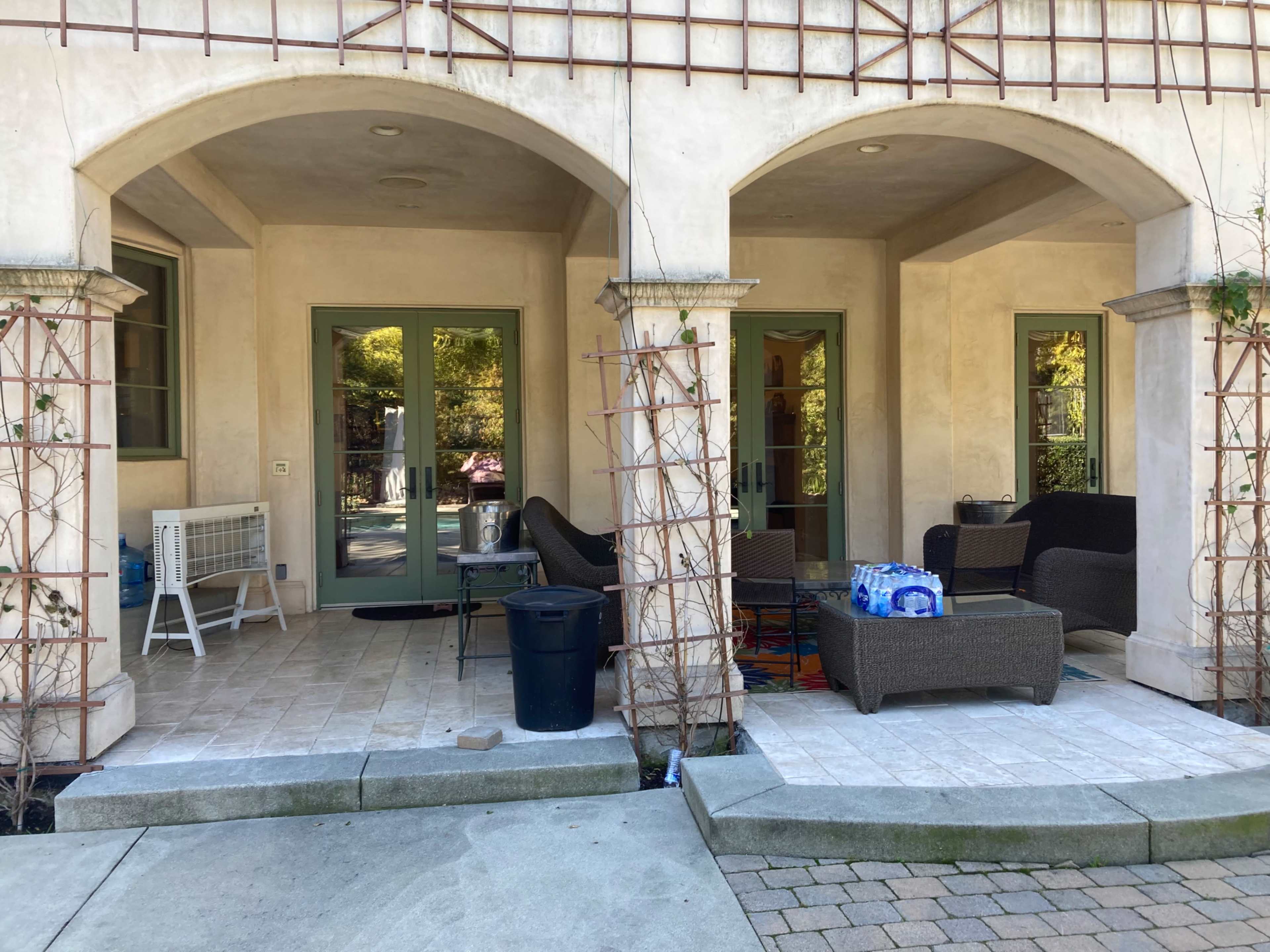 The image shows a patio area with arched entrances, featuring outdoor furniture and potted plants.