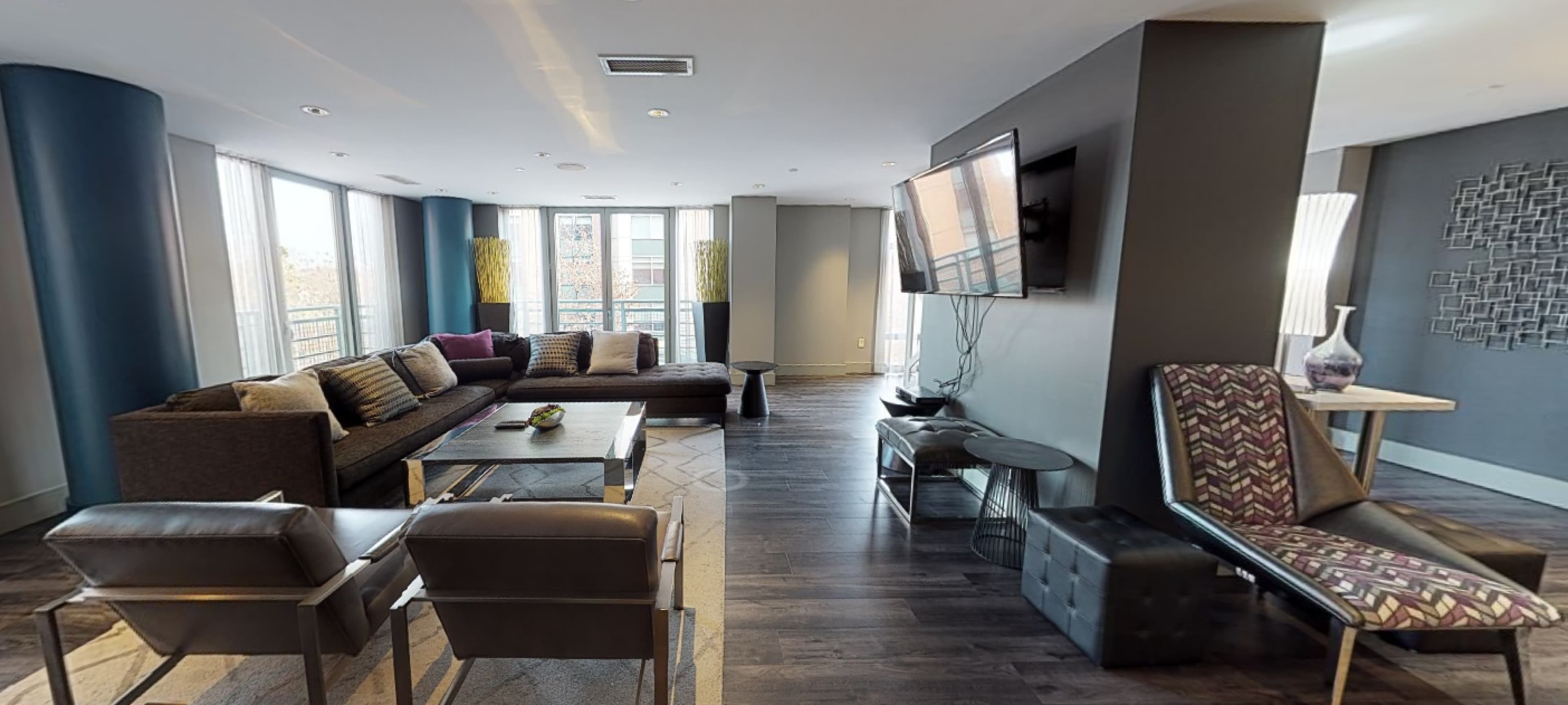 The image shows a modern, open-concept living area featuring a sectional sofa, armchairs, a coffee table, and a television mounted on the wall.