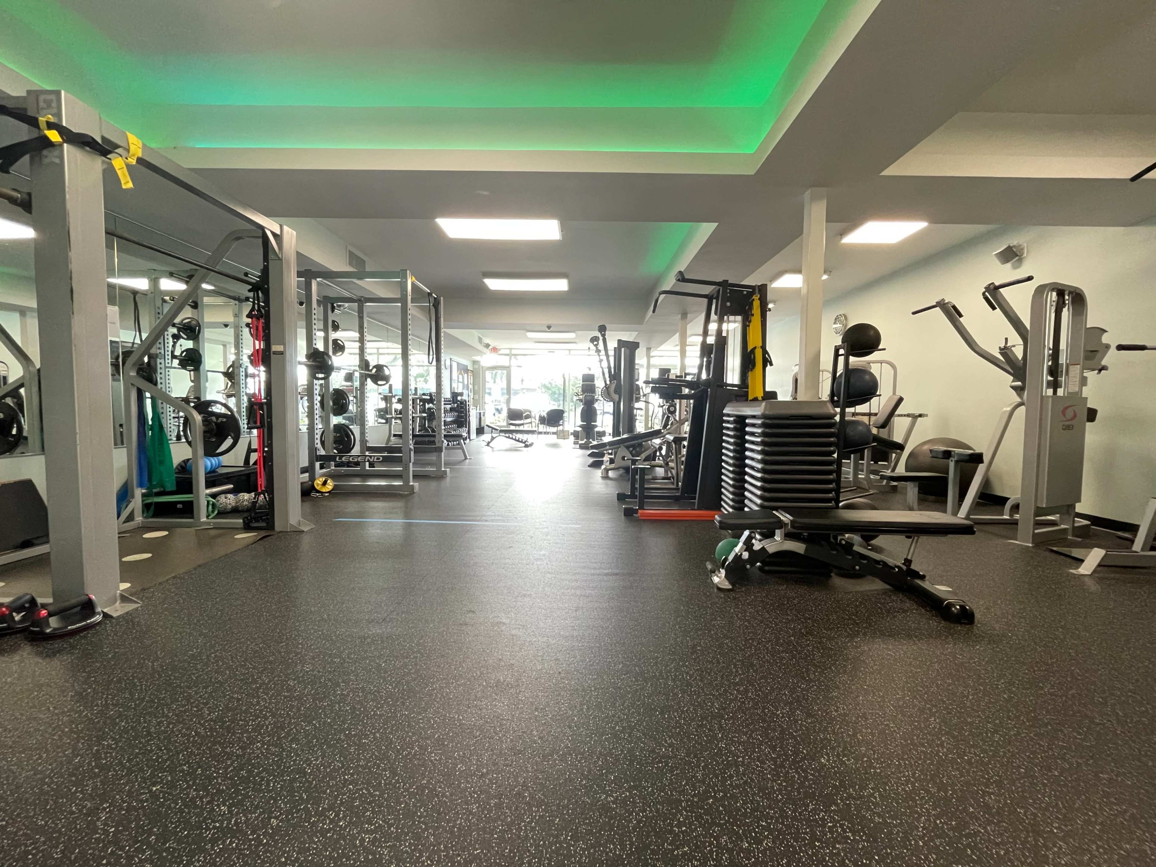 The image shows a modern gym interior featuring various exercise equipment arranged neatly along the space.