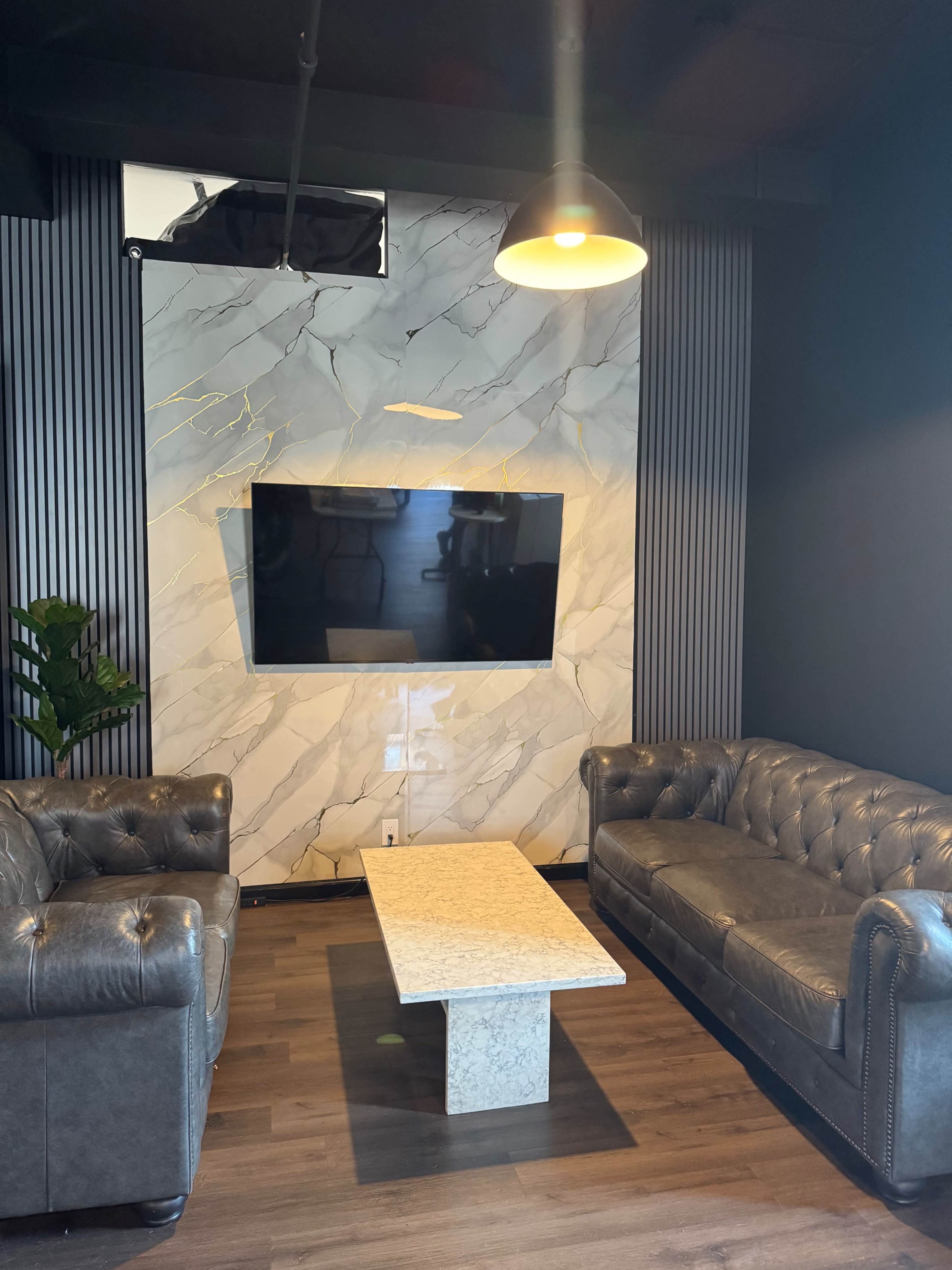 The image shows a modern lounge area with two leather sofas facing a stone coffee table and a wall-mounted television above a marble accent wall.