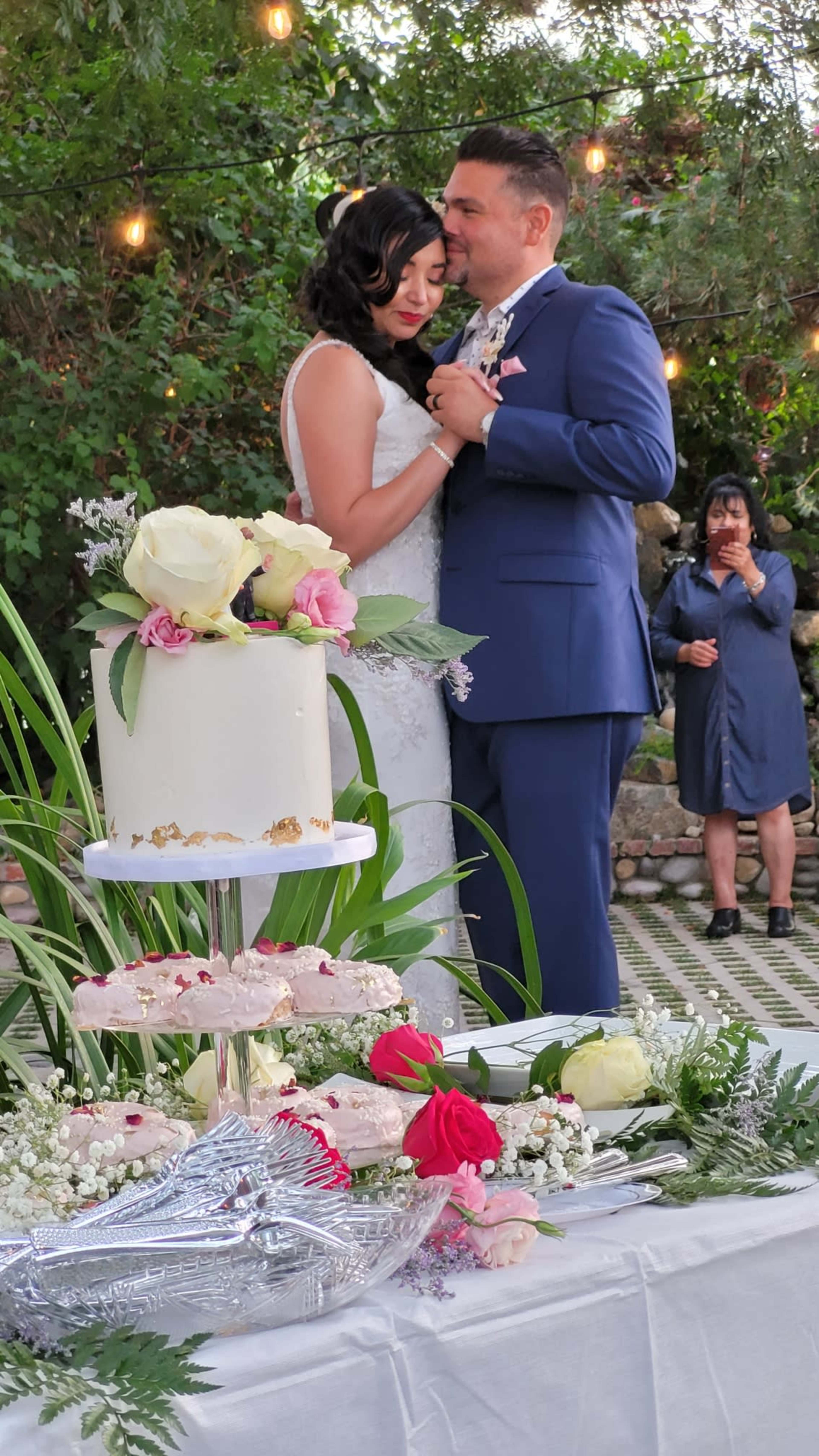 A couple dances together at their wedding reception, with a decorated cake and floral arrangements in the foreground.
