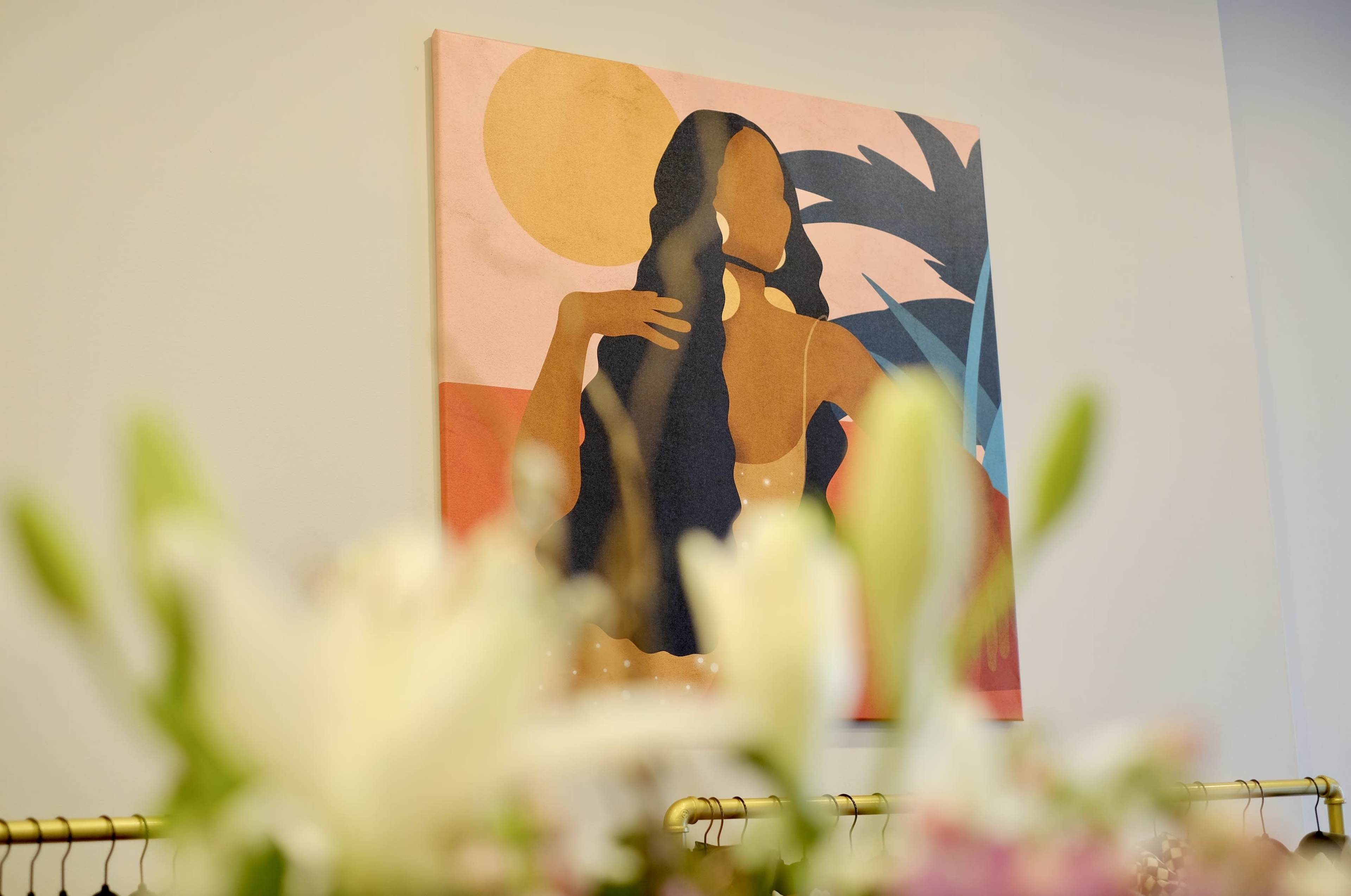 A painting featuring a woman with long hair is displayed on a wall, partially obscured by flowers in the foreground.