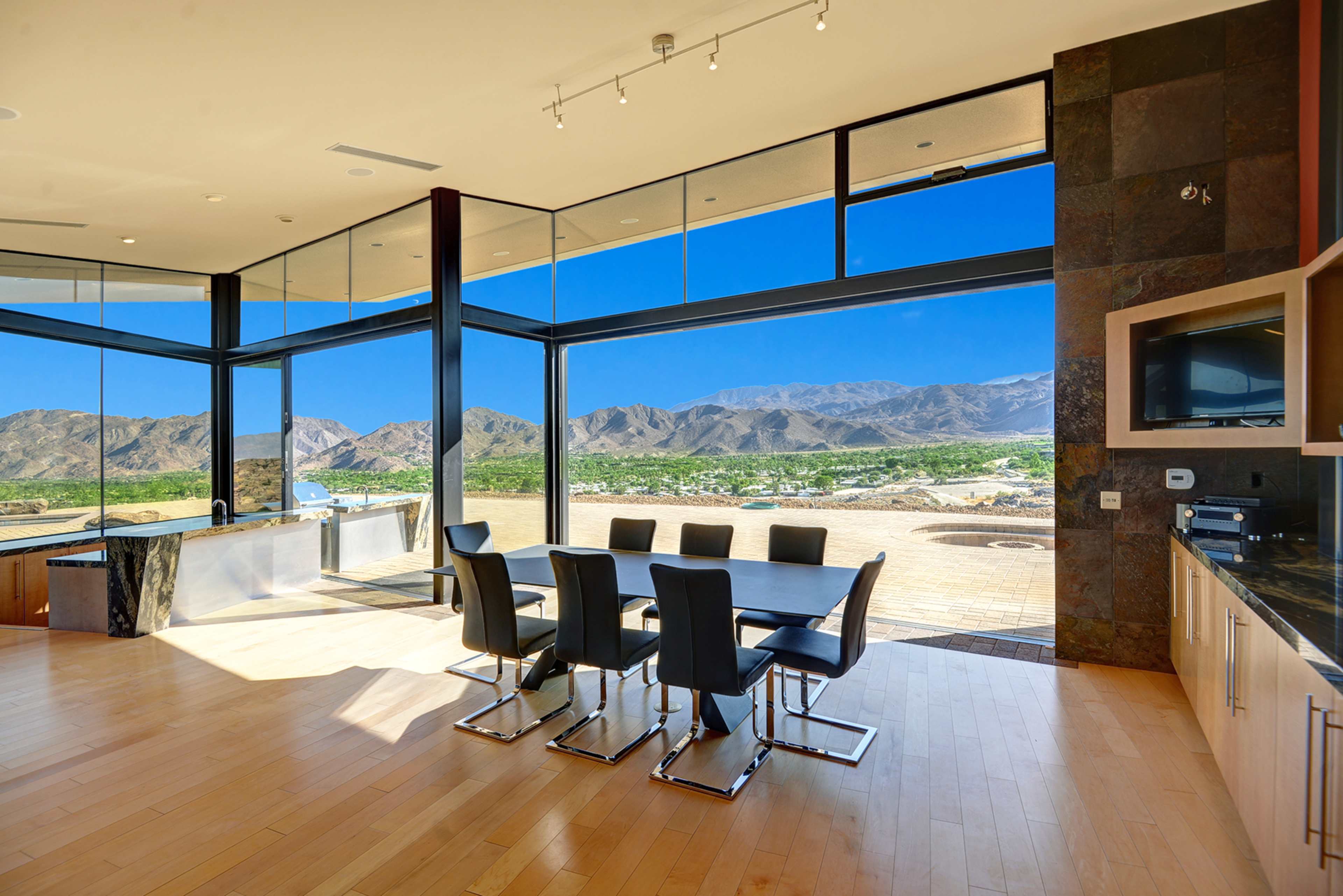A modern dining area features a large table with black chairs and expansive windows showcasing a mountain view.