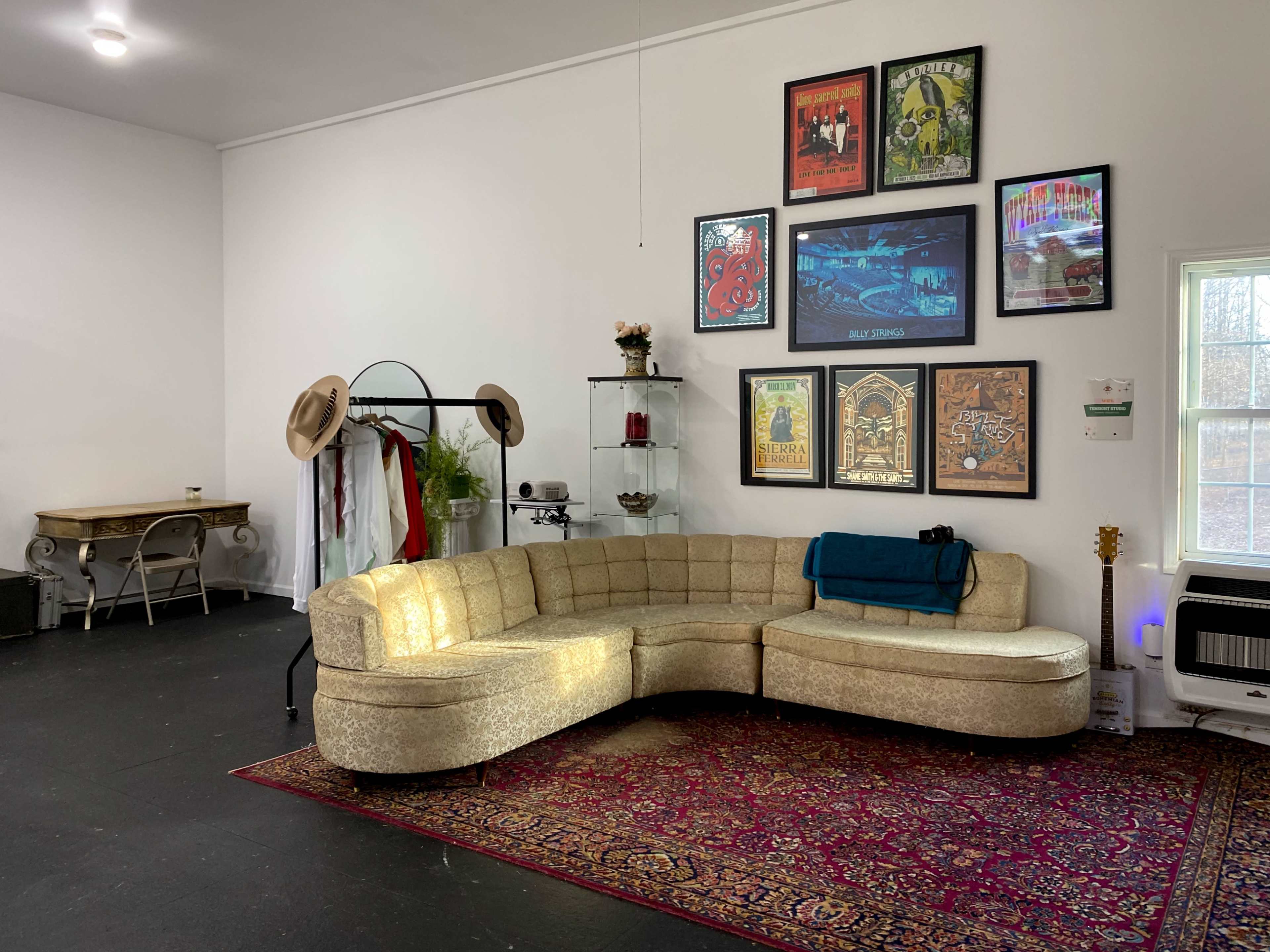 The image shows a spacious room featuring a curved golden sofa, a patterned rug, wall art, and a small table with decorative items.