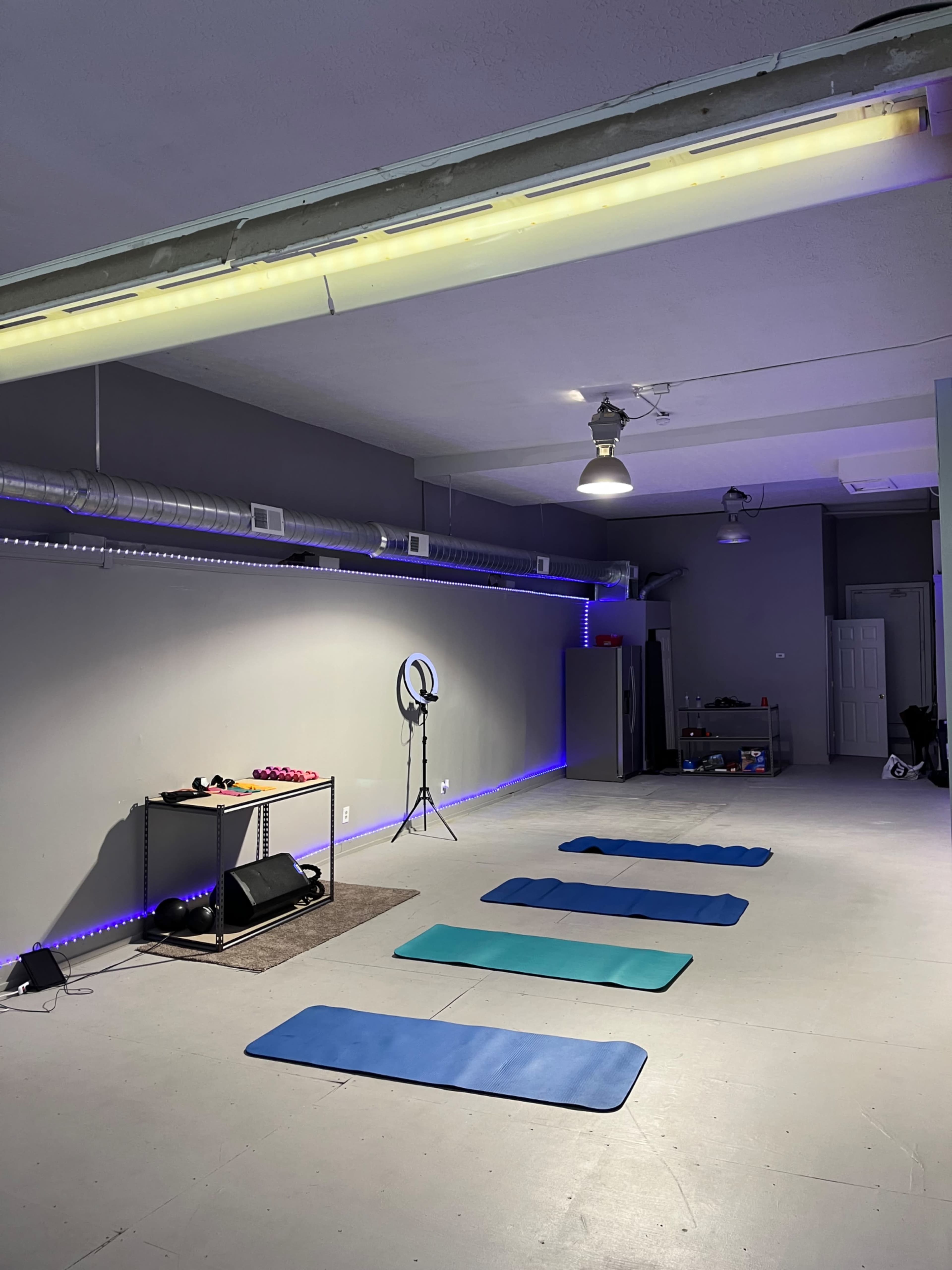 A spacious yoga or exercise studio with several mats arranged on the floor, a mirror, and lights along the walls.