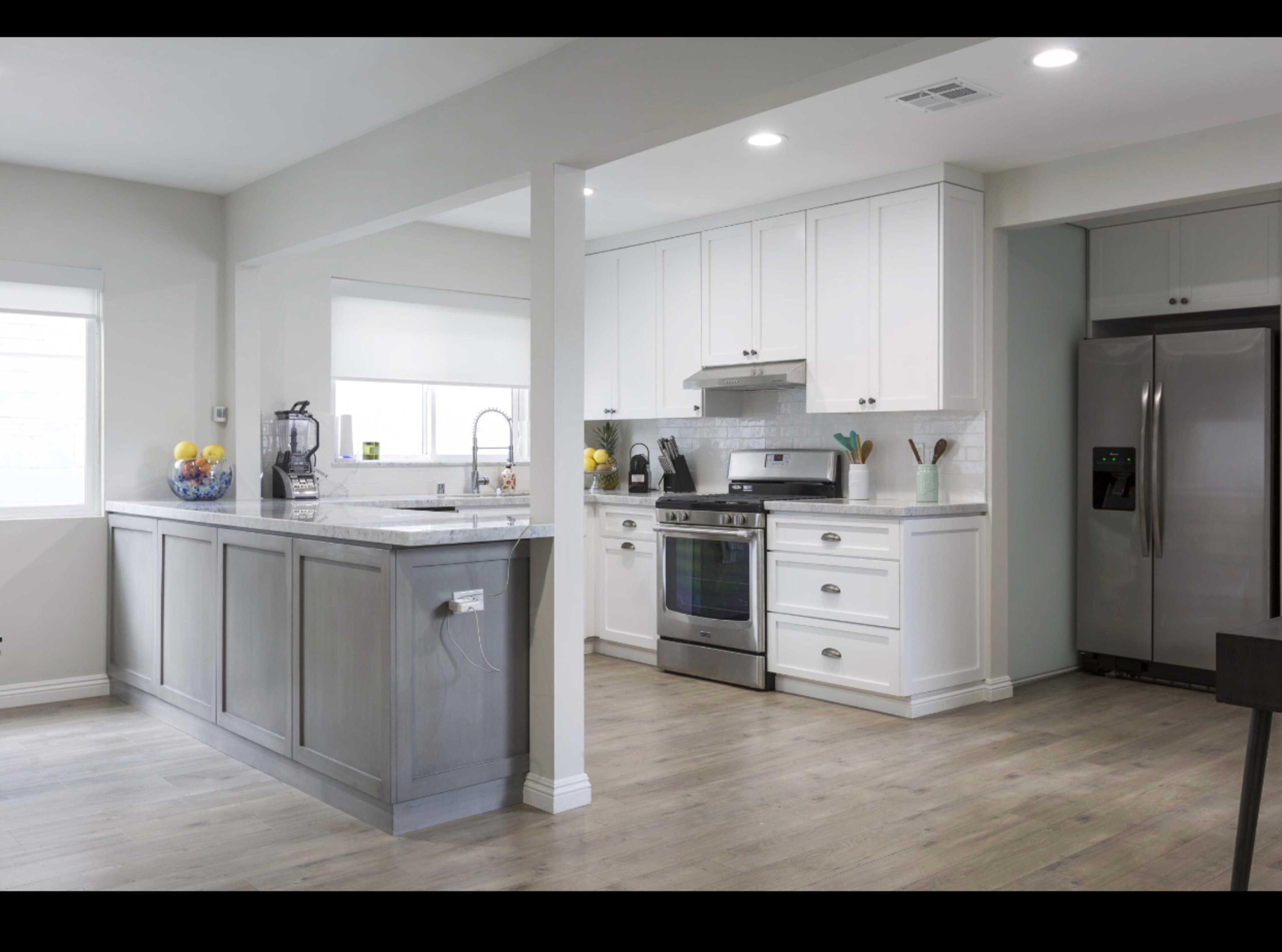 A modern kitchen features white cabinetry, stainless steel appliances, and a gray island with a countertop, surrounded by light wood flooring.