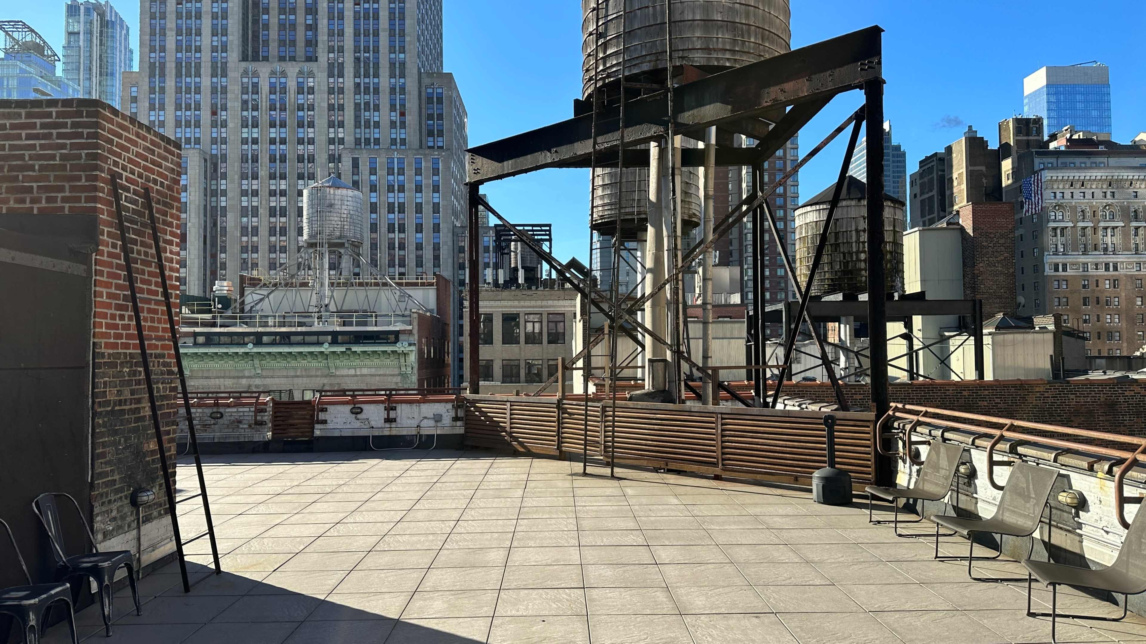 The image features an urban rooftop scene with a flat terrace, water towers, and surrounding skyscrapers under a clear blue sky.