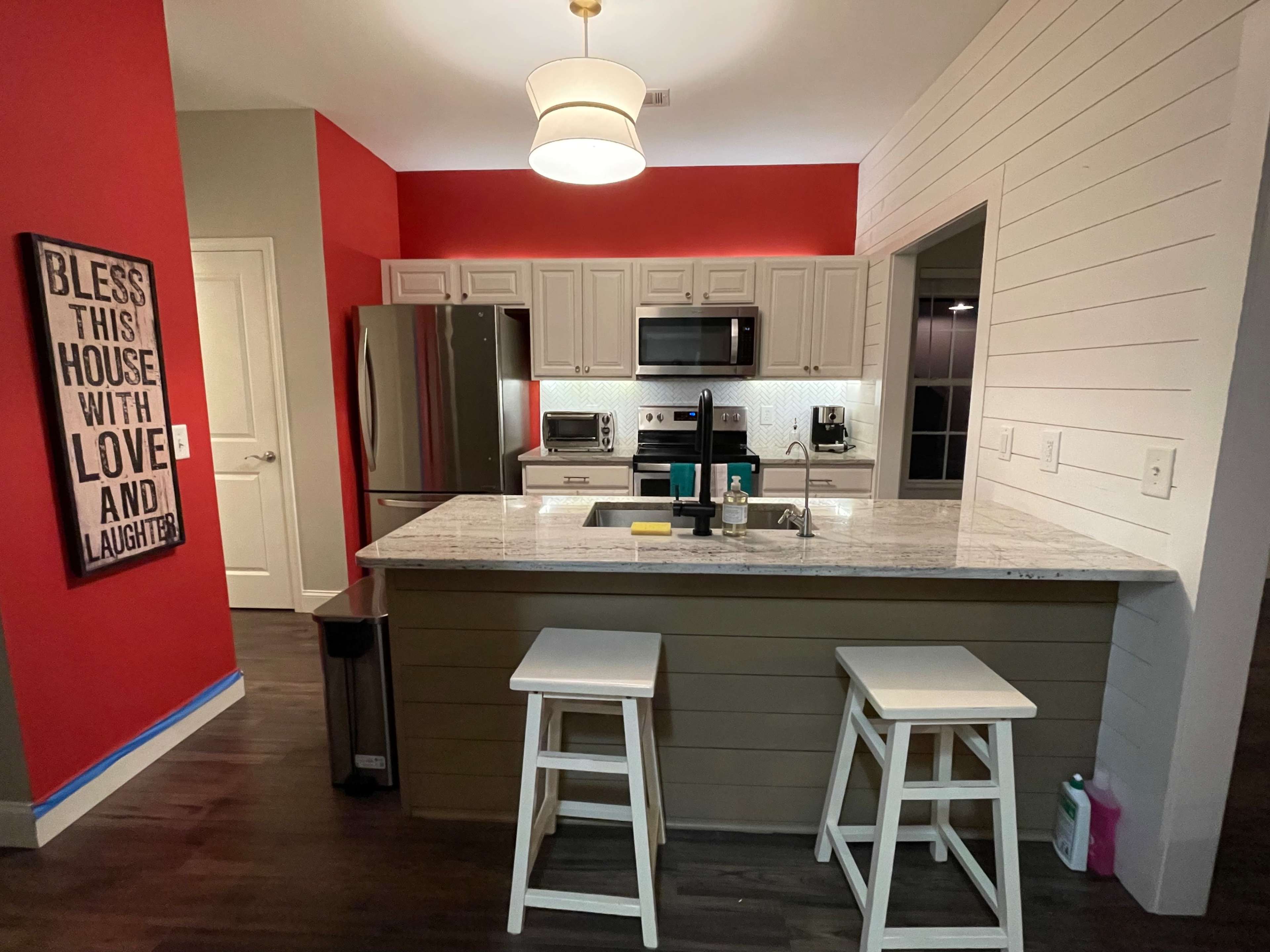 A modern kitchen with a granite countertop island, white cabinetry, stainless steel appliances, and a red accent wall.