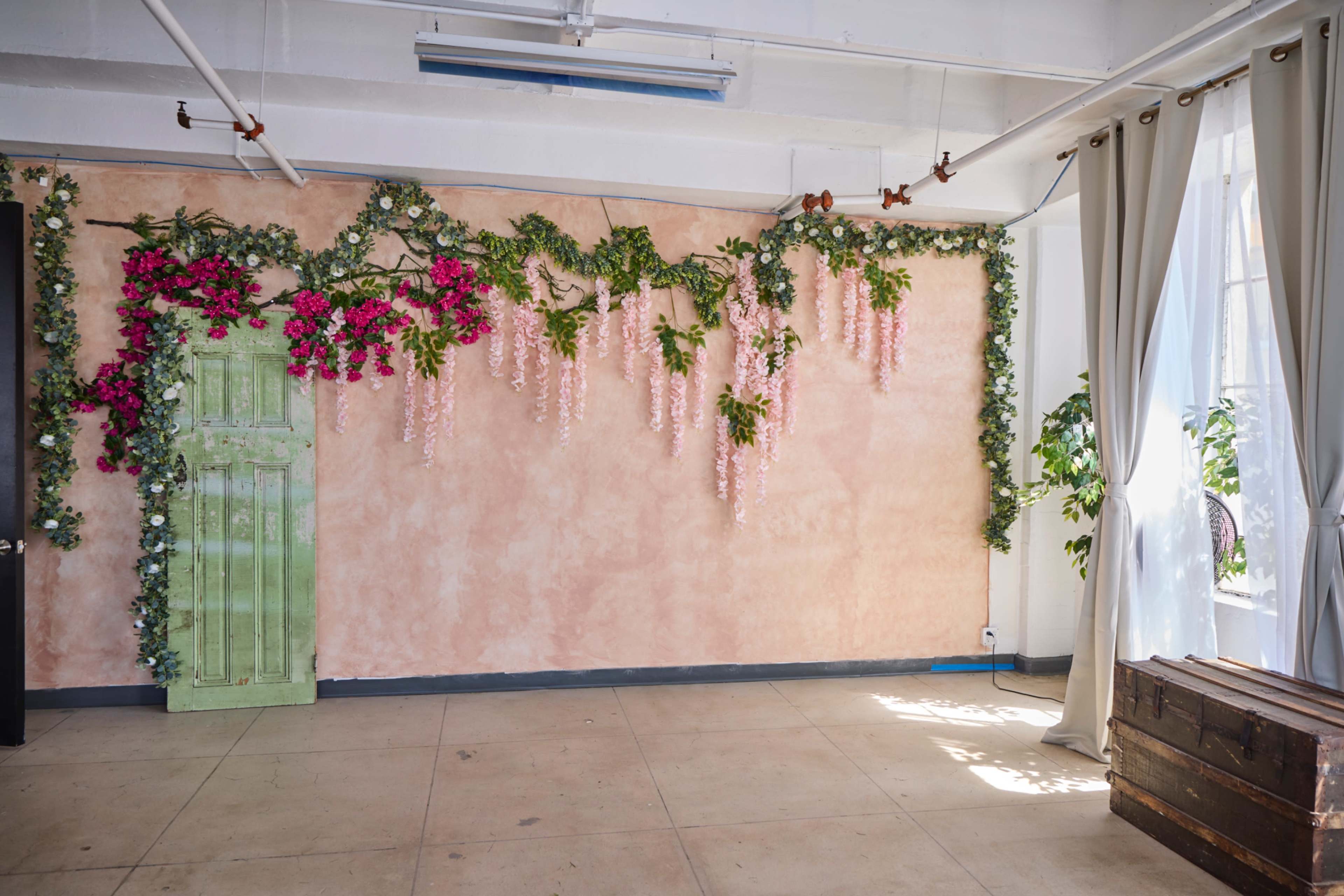 A room with a pink wall adorned with green vines and pink flowers, a green door, and a wooden box in the corner.