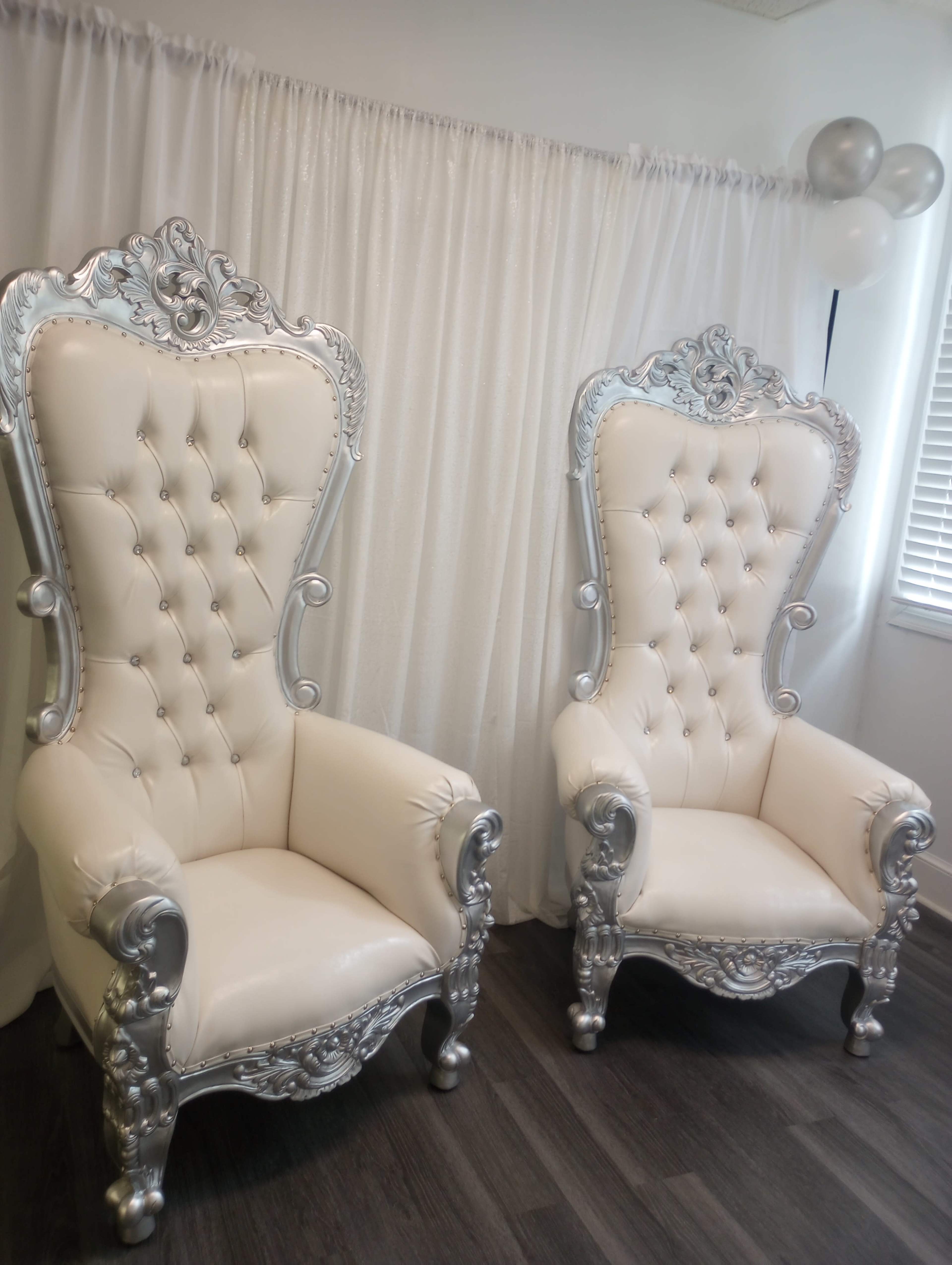 Two ornate white chairs with silver accents, positioned side by side against a white backdrop.