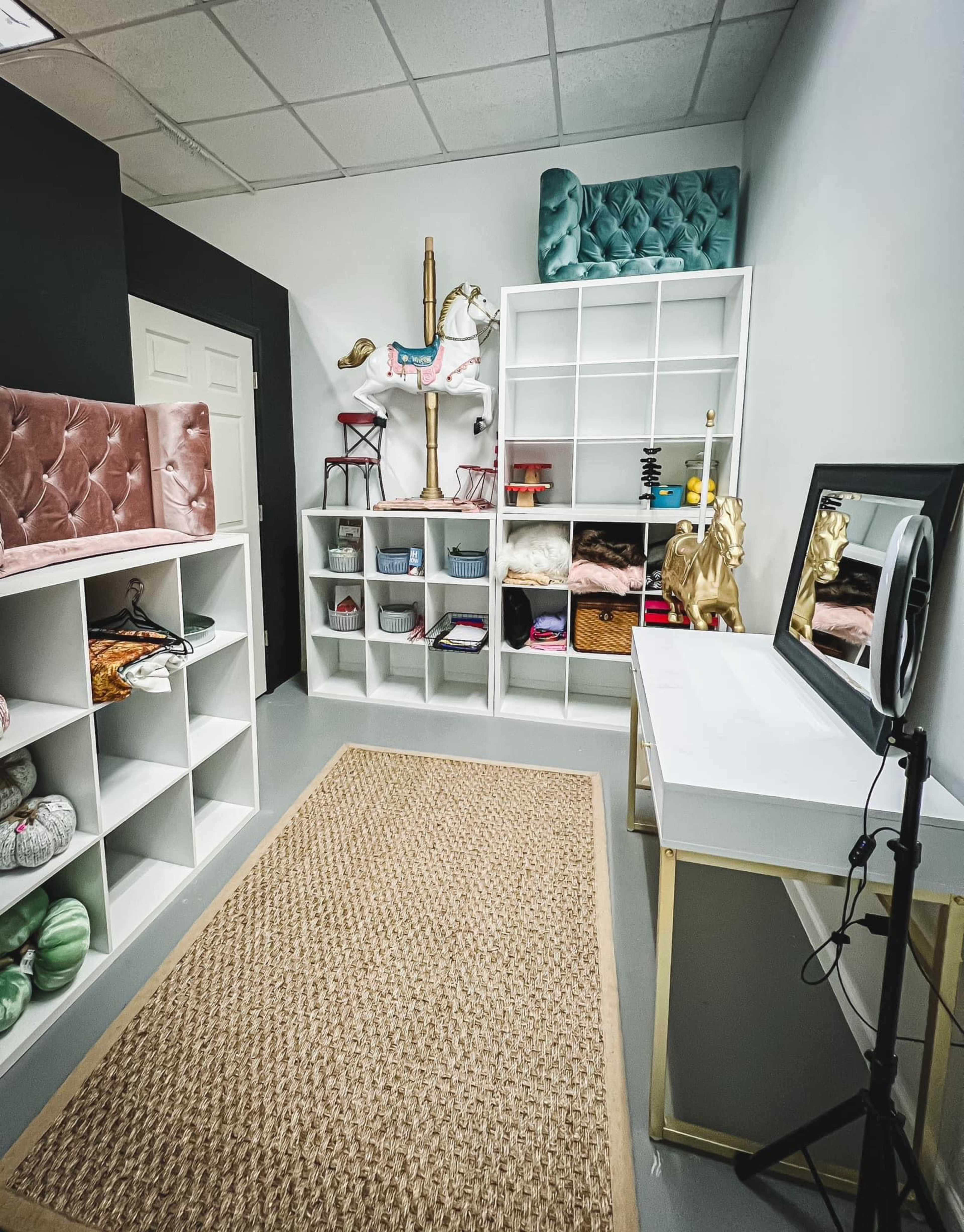 The image shows a well-organized room with white shelves filled with various items, a small vanity table, and decorative elements including a horse statue and plush seating.