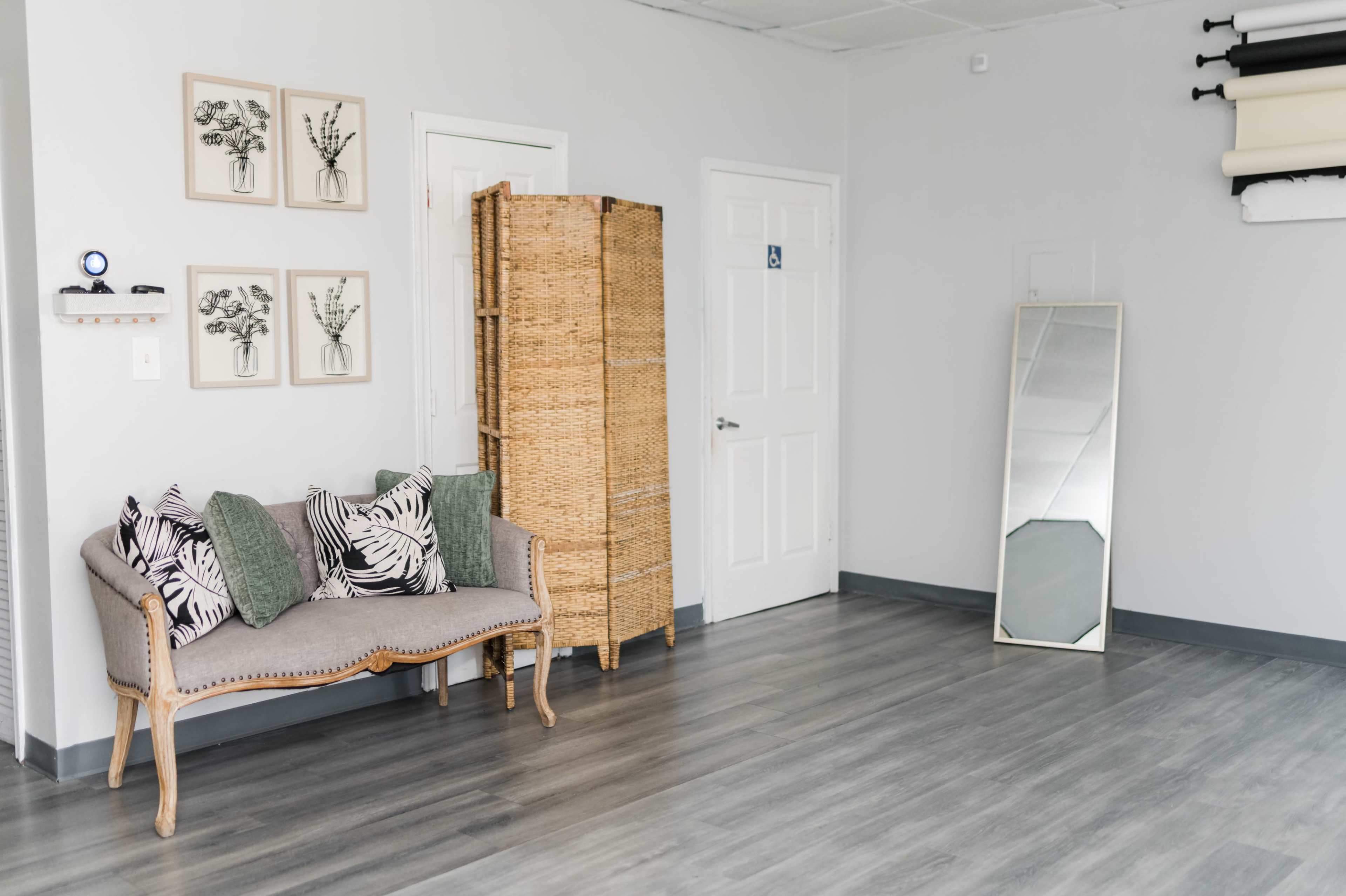 A minimalist interior with a couch, decorative framed artworks on the wall, a wicker screen, and a full-length mirror.