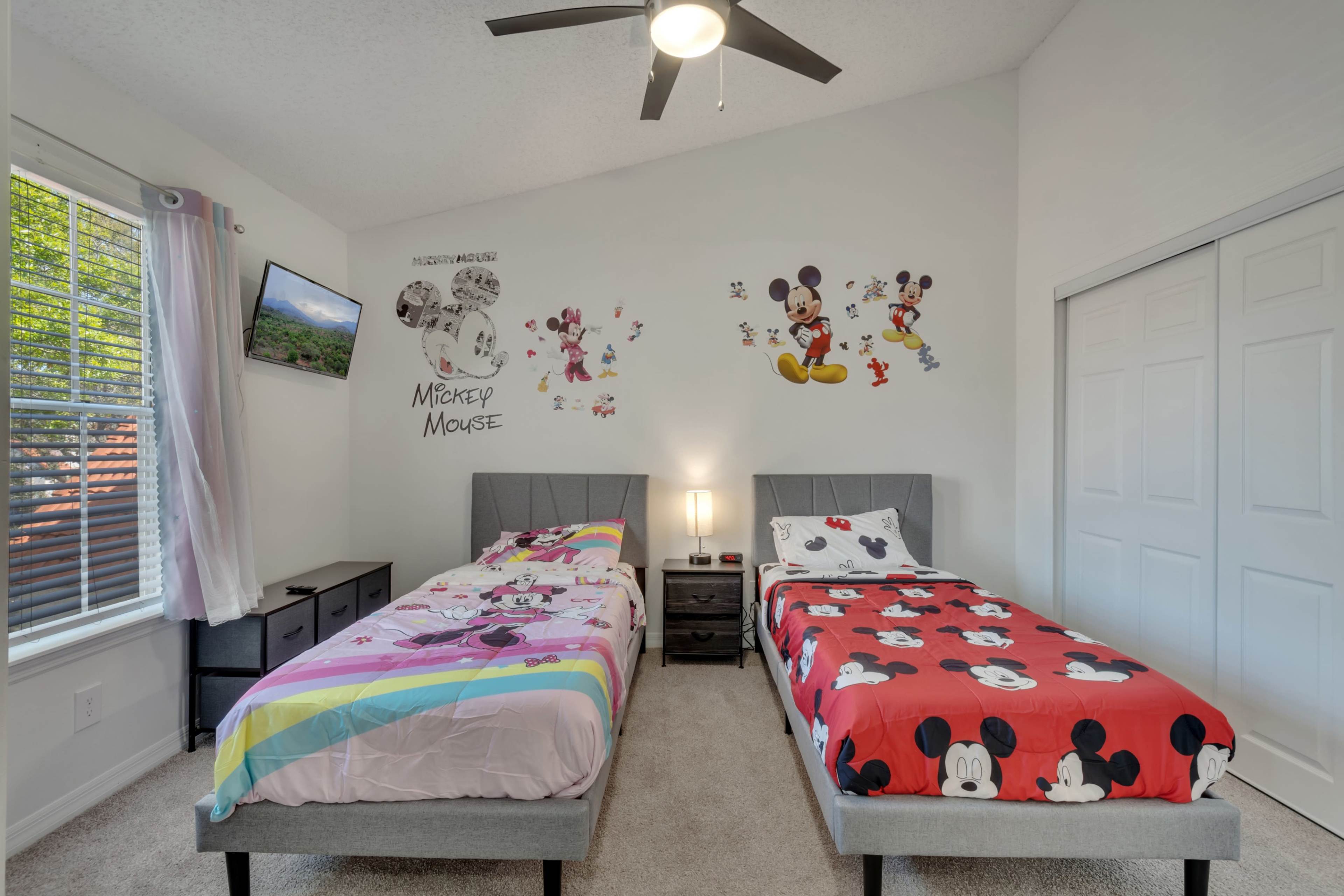 The room features two beds with themed bedding, a small TV on the wall, and Mickey Mouse decorations.