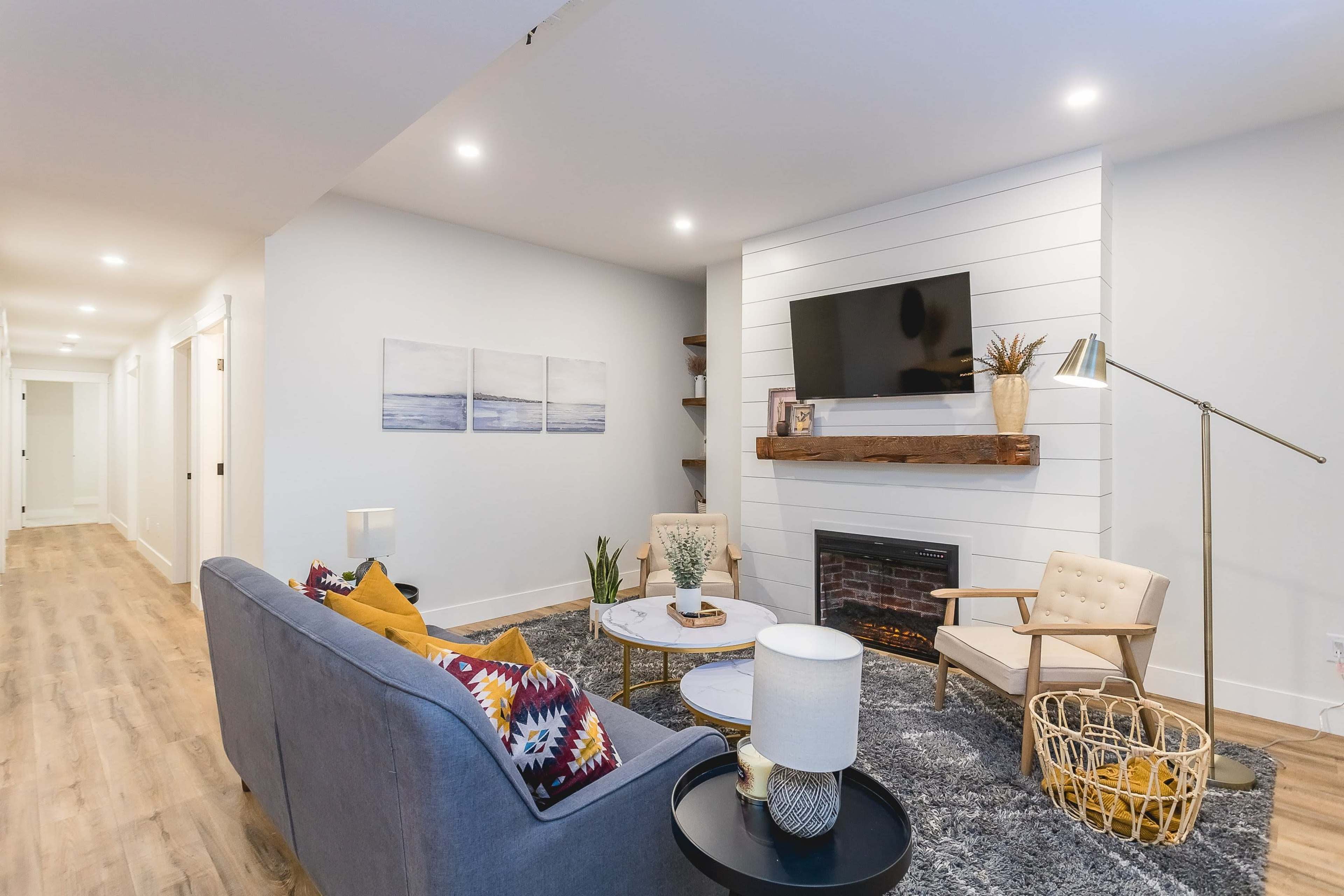 A modern living room with a gray sofa, a coffee table, a mounted television above a white shiplap fireplace, and a cozy reading chair.