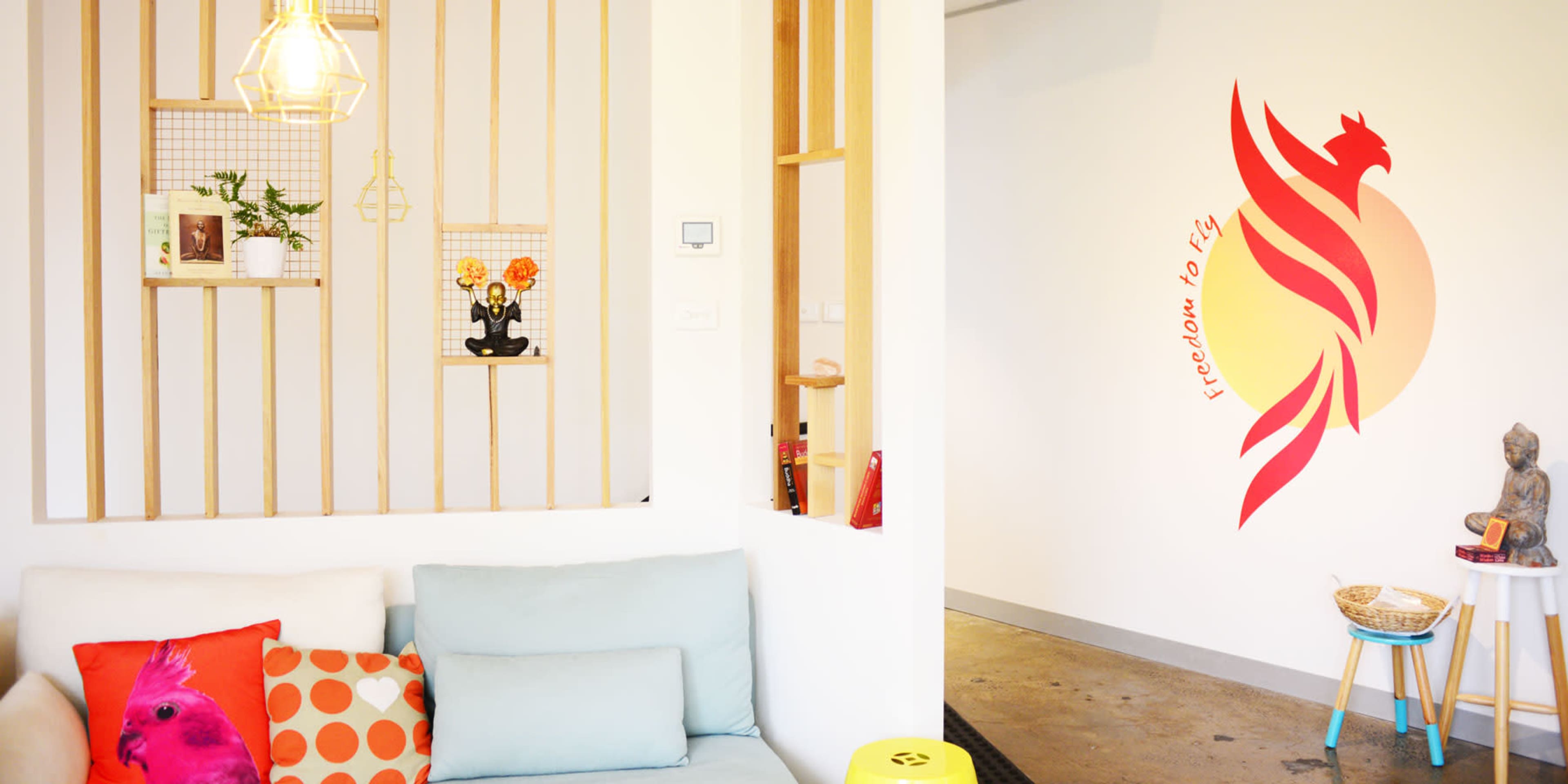 A cozy interior space featuring a light blue couch, decorative wall designs, and a vibrant mural of a phoenix with the phrase "freedom to fly."