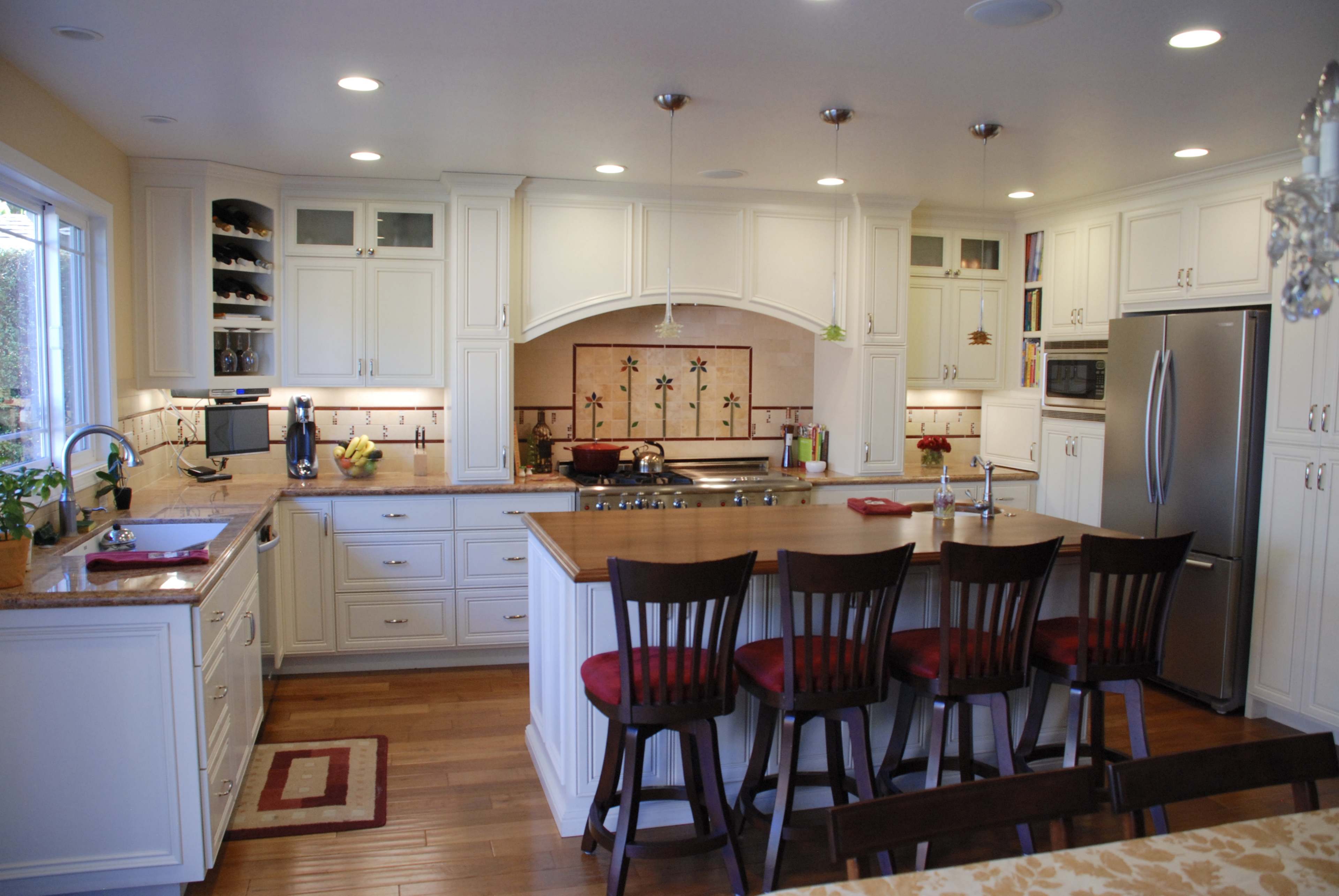 A modern kitchen features white cabinetry, a central island with bar stools, and stainless steel appliances.