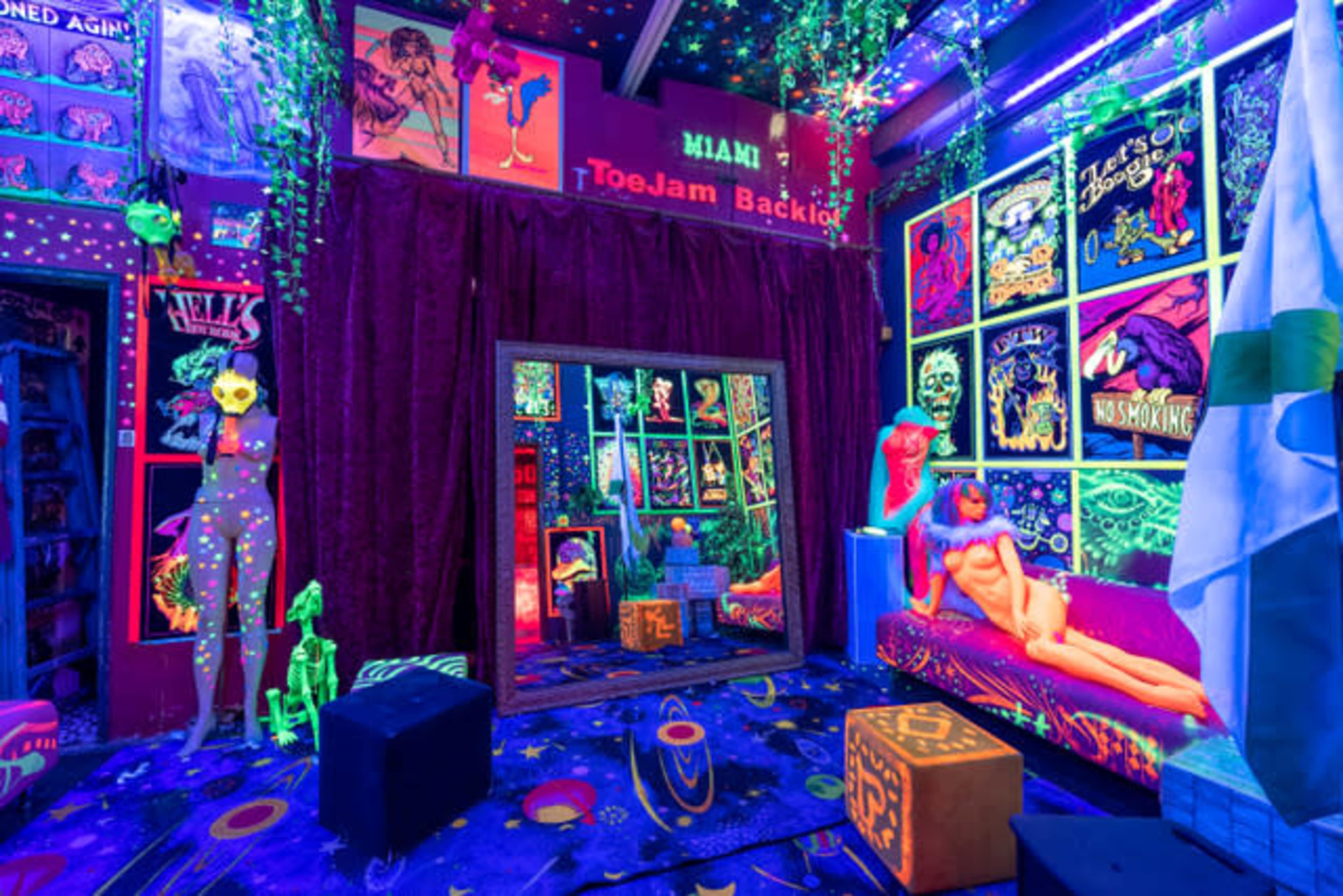 A vibrant, neon-colored room filled with psychedelic art, plush seating, and decorative plants, illuminated by blacklight.