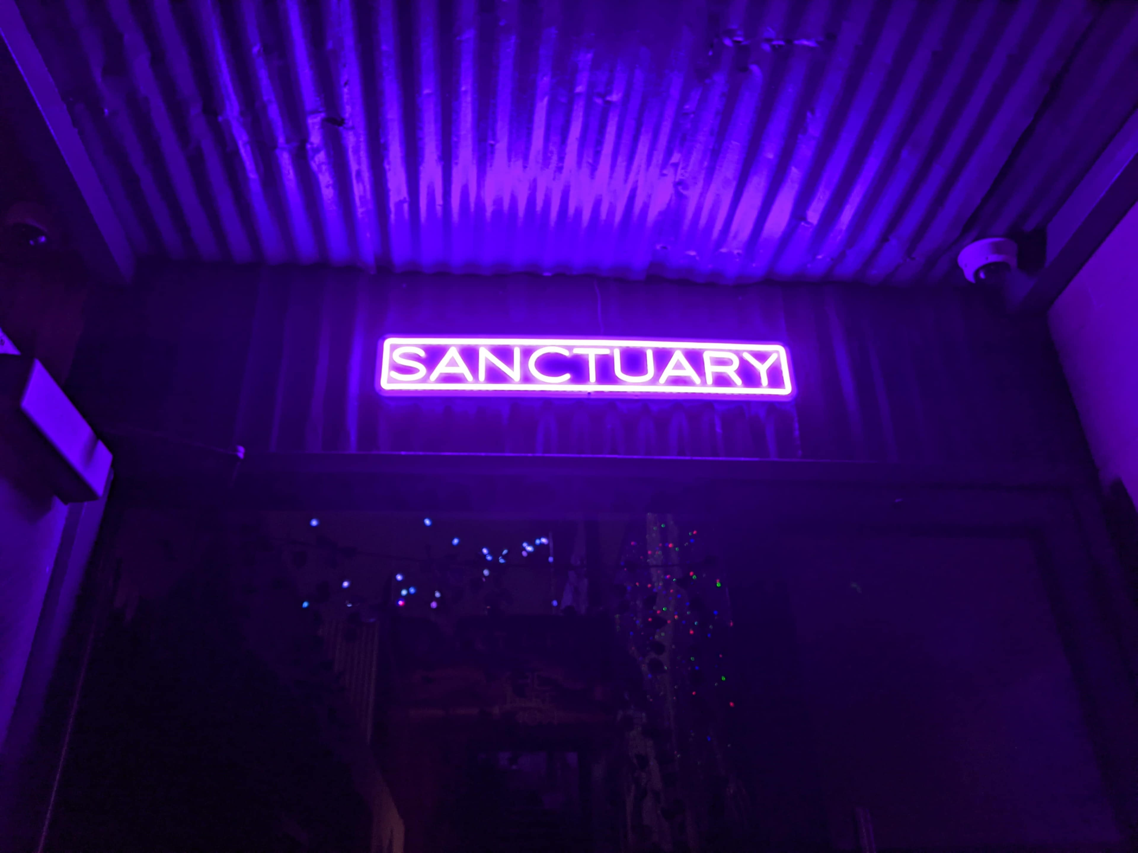 A brightly lit purple neon sign displays the word "SANCTUARY" above an entrance.