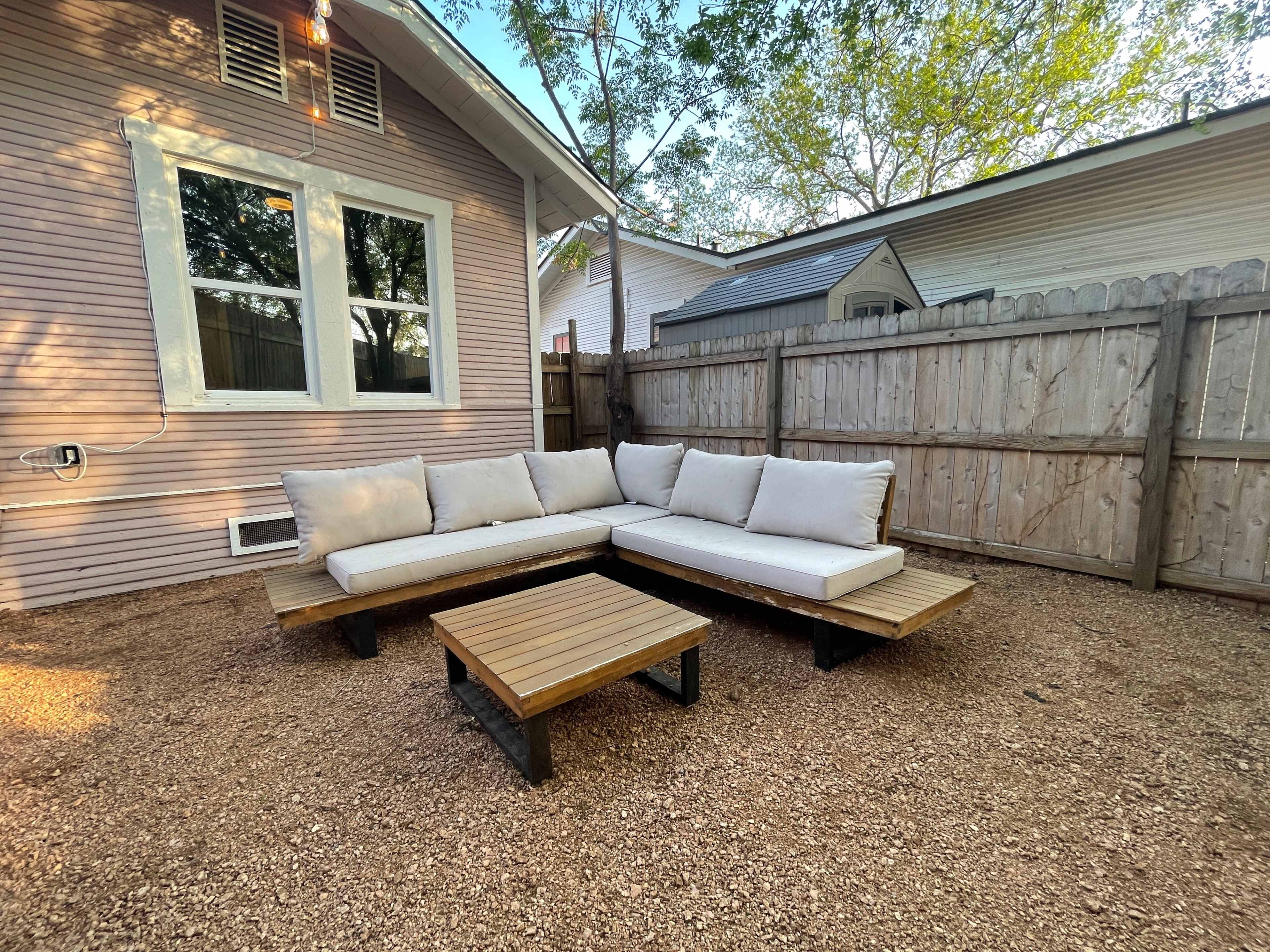 A sectional outdoor seating arrangement with a matching coffee table on a gravel surface in a fenced backyard.