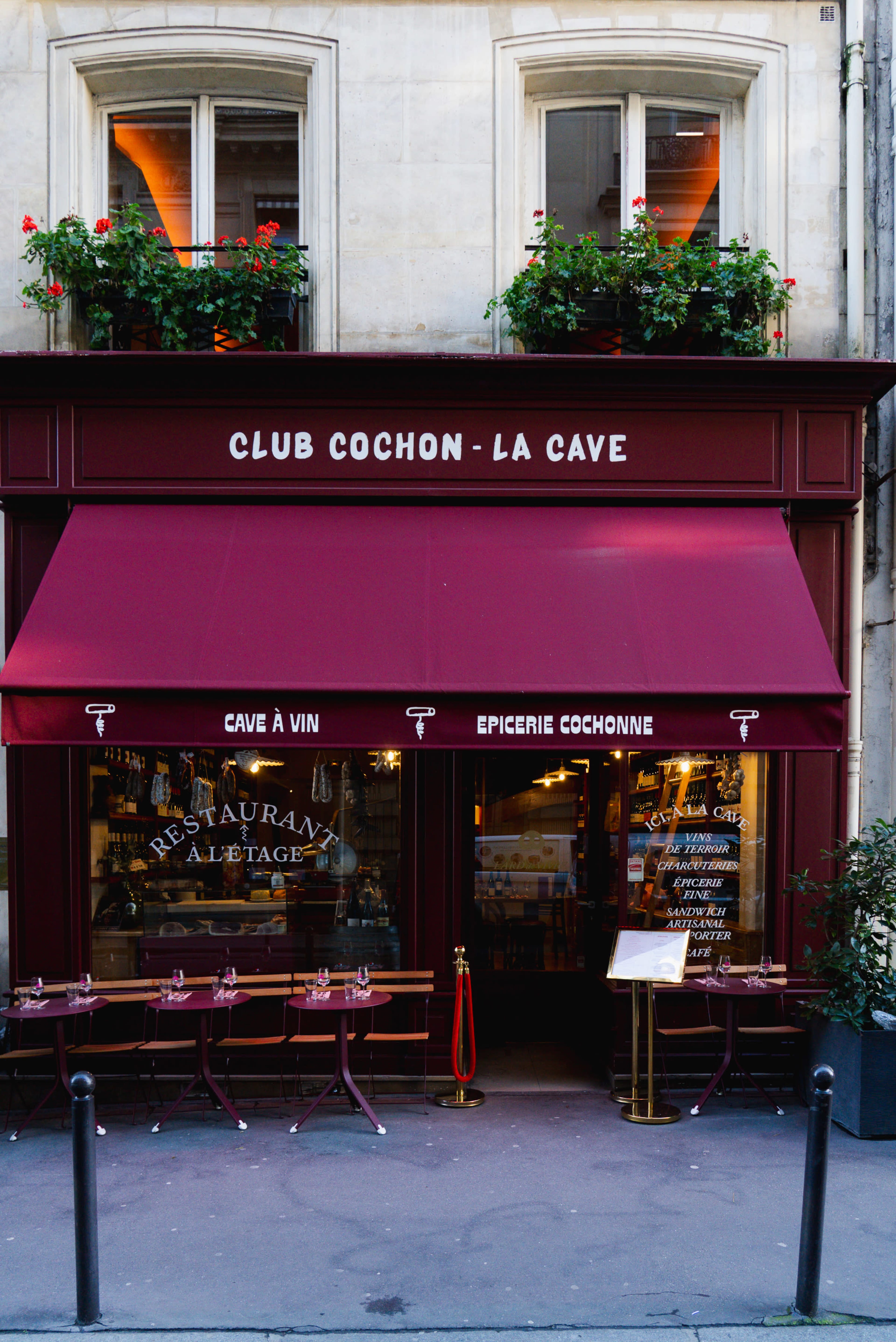 The image features a storefront of a restaurant called "Club Cochon - La Cave," with red awnings and outdoor seating in front.