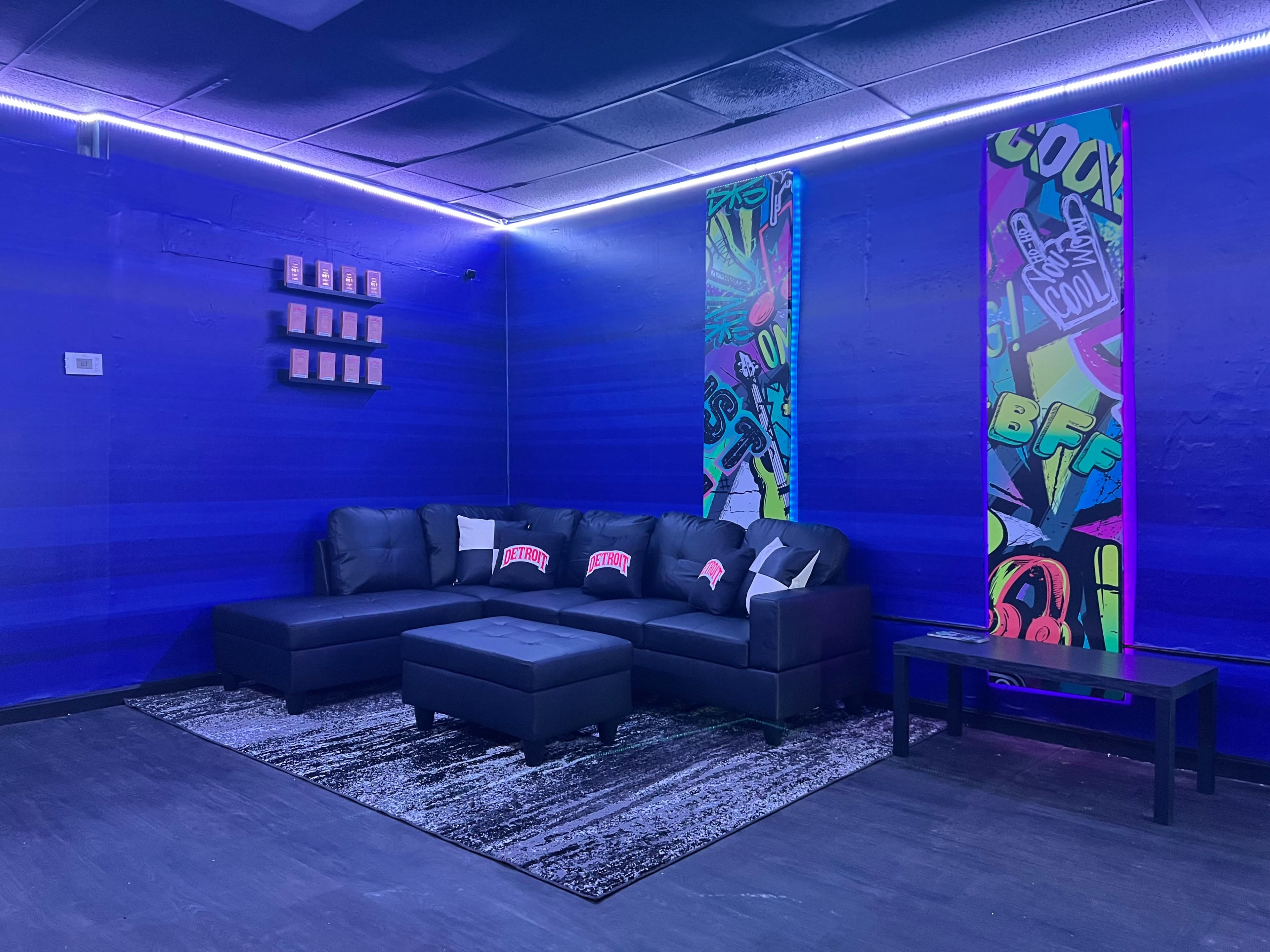 A blue-themed lounge area with a black sectional sofa, an ottoman, a dark table, and colorful wall art featuring playful graphics.