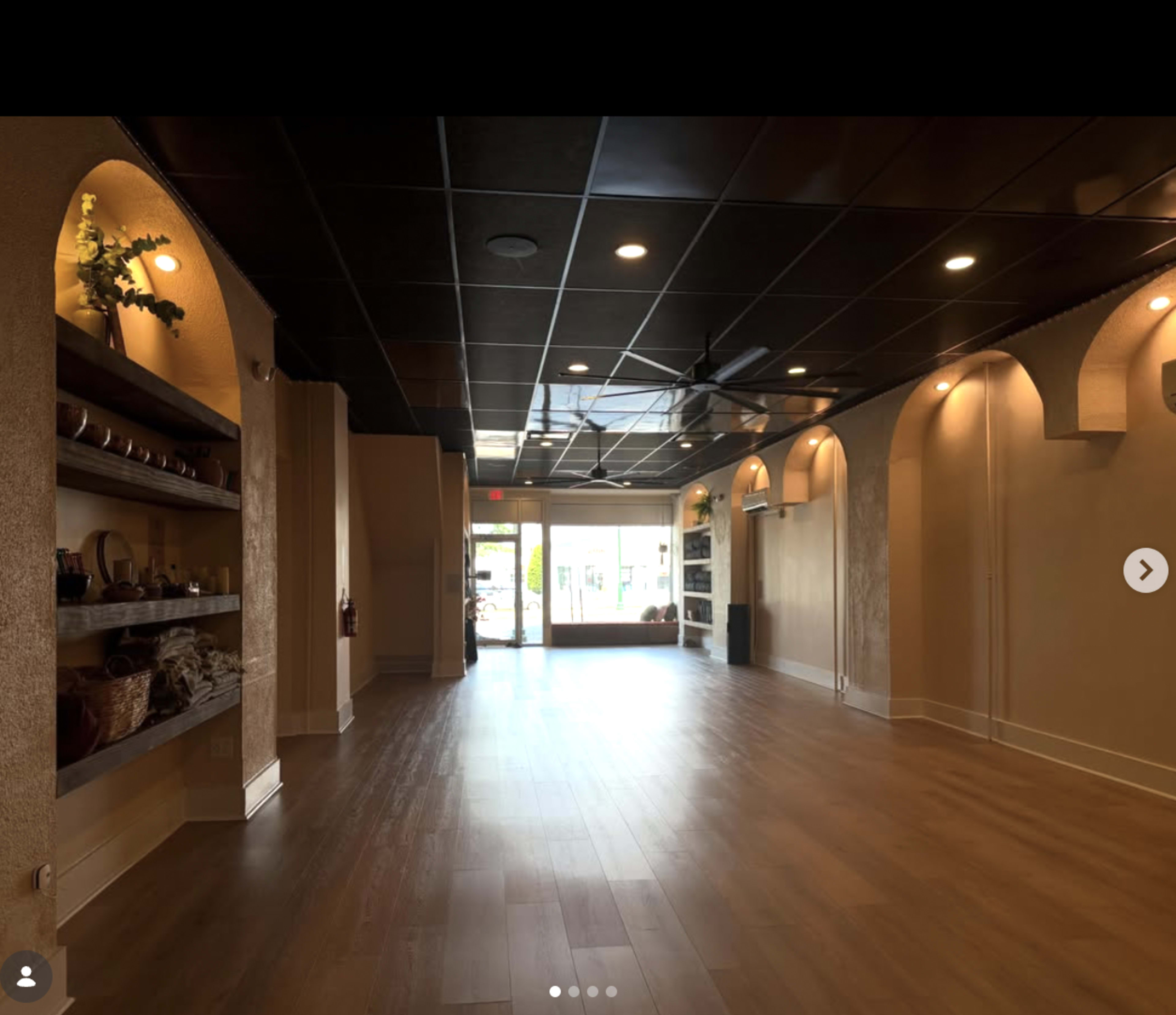 The image shows a spacious, empty interior of a commercial space with shelves on the walls and large windows at the entrance.