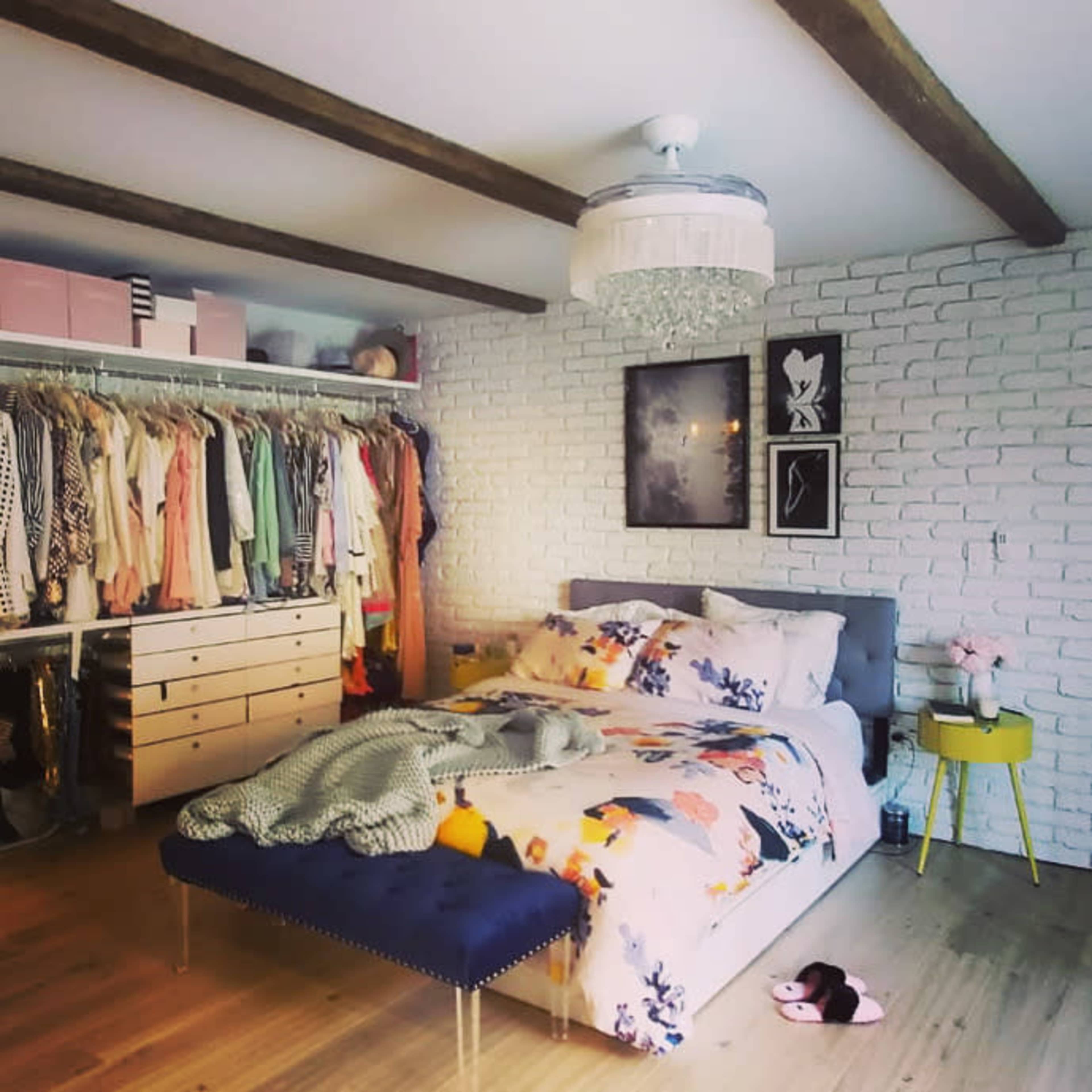 A well-organized bedroom featuring a bed with floral bedding, a closet filled with clothing, and a chandelier hanging from the ceiling.