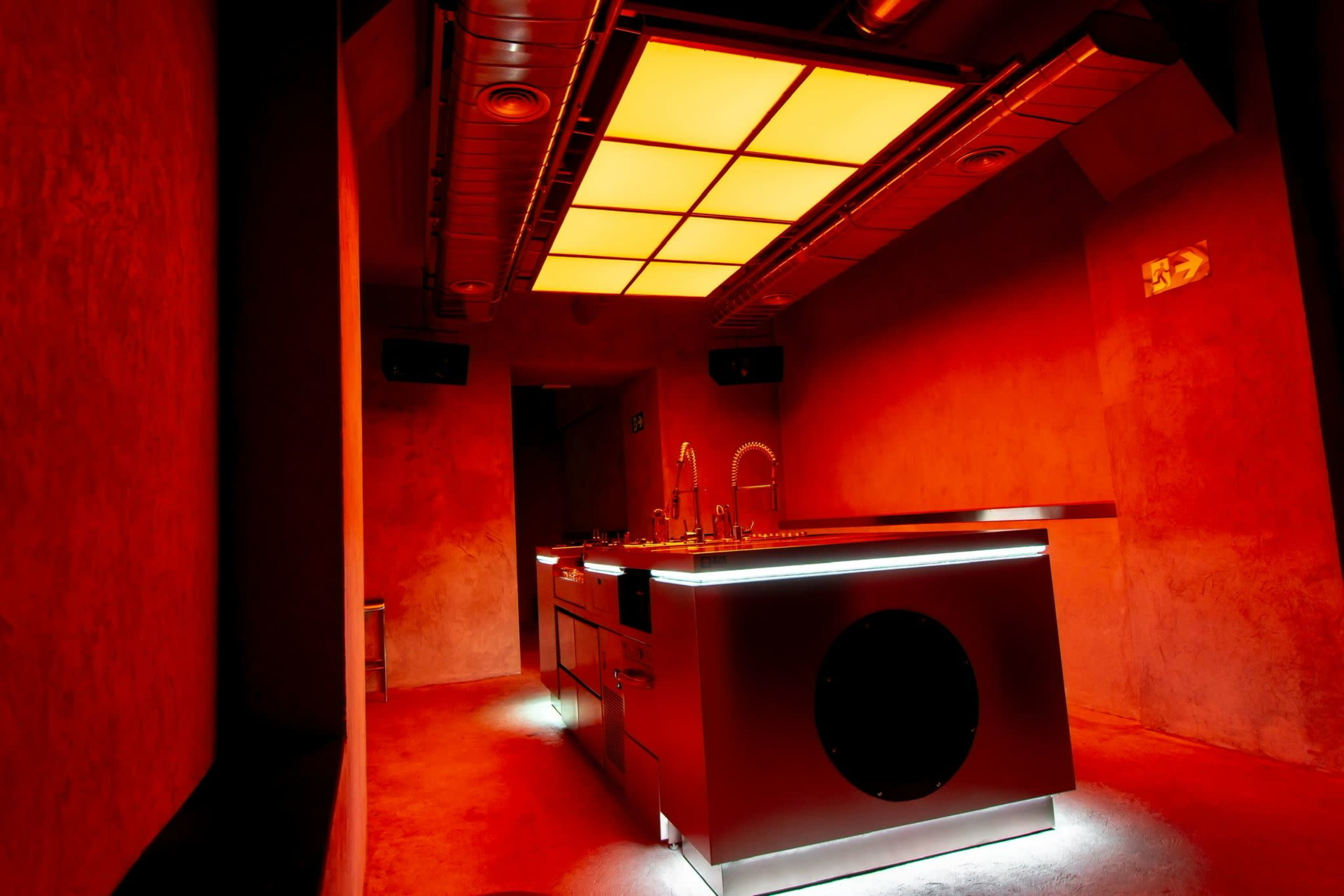A sleek, modern kitchen with a bright, illuminated ceiling and red-tinted walls, featuring a prominent kitchen island.