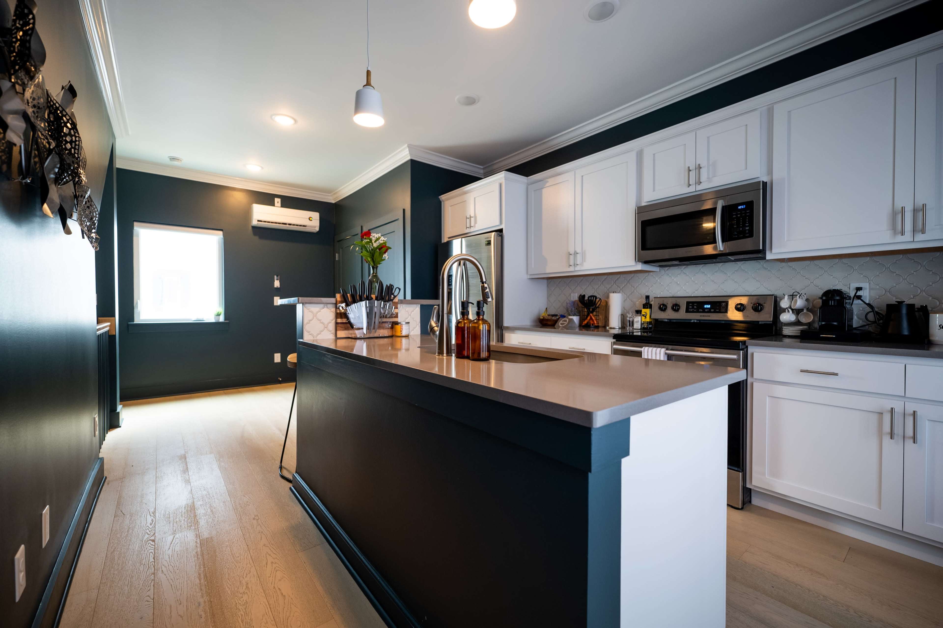 The image shows a modern kitchen with white cabinets, stainless steel appliances, and a dark green accent wall.