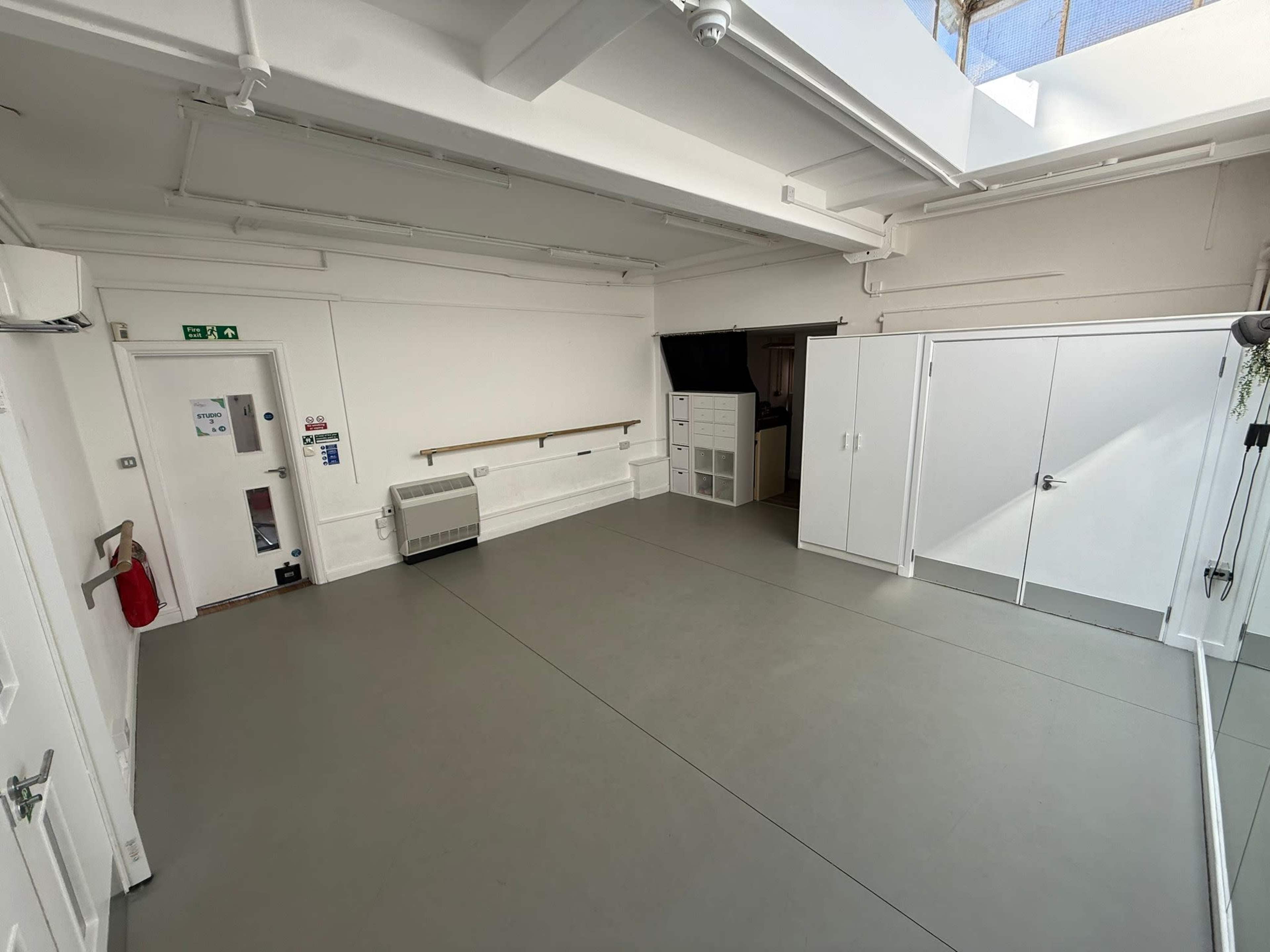 The image shows a spacious, minimalist studio with white walls, a skylight, and a light gray floor.