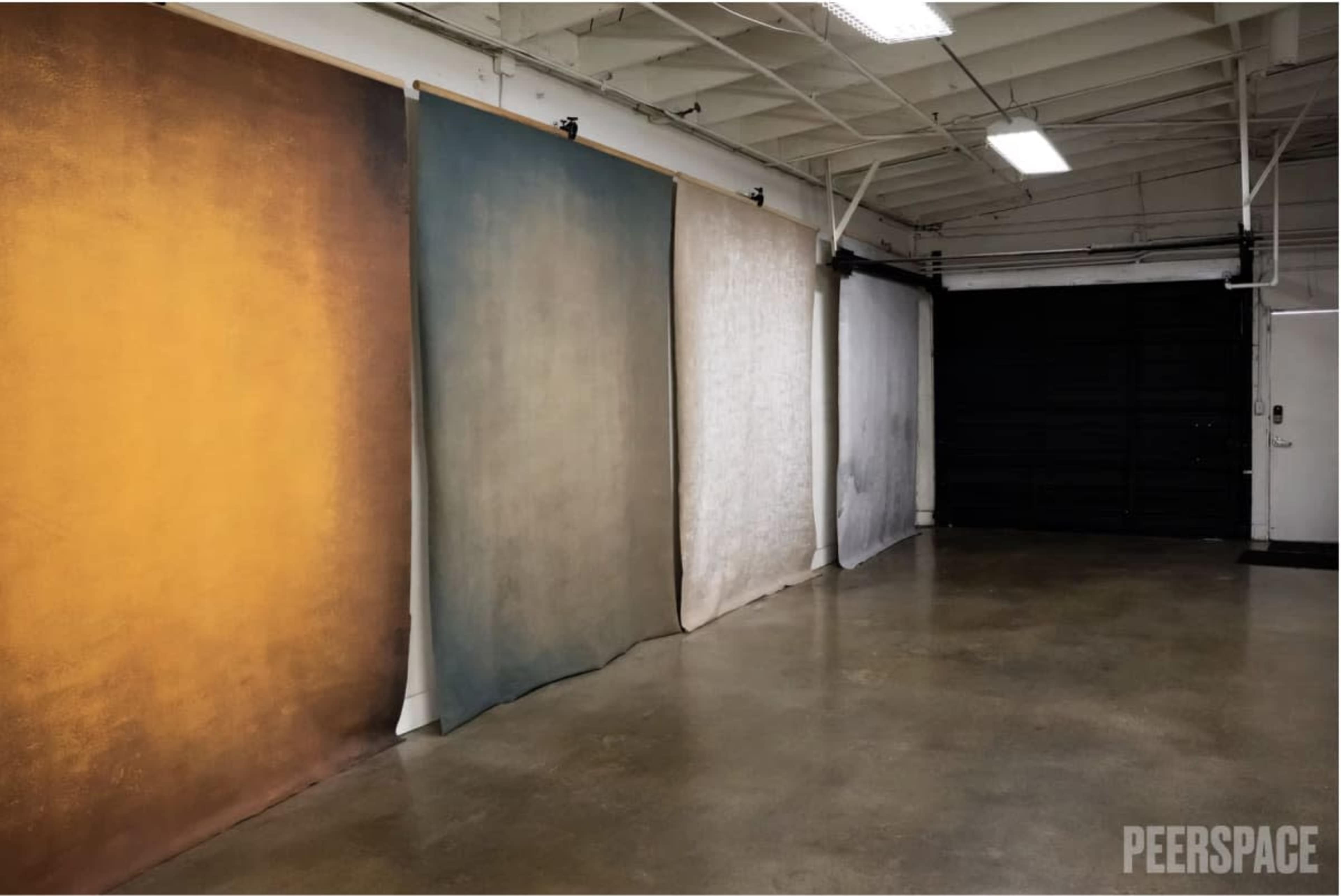 The image shows a spacious studio with several large backdrops hanging from the ceiling, positioned against a polished concrete floor.