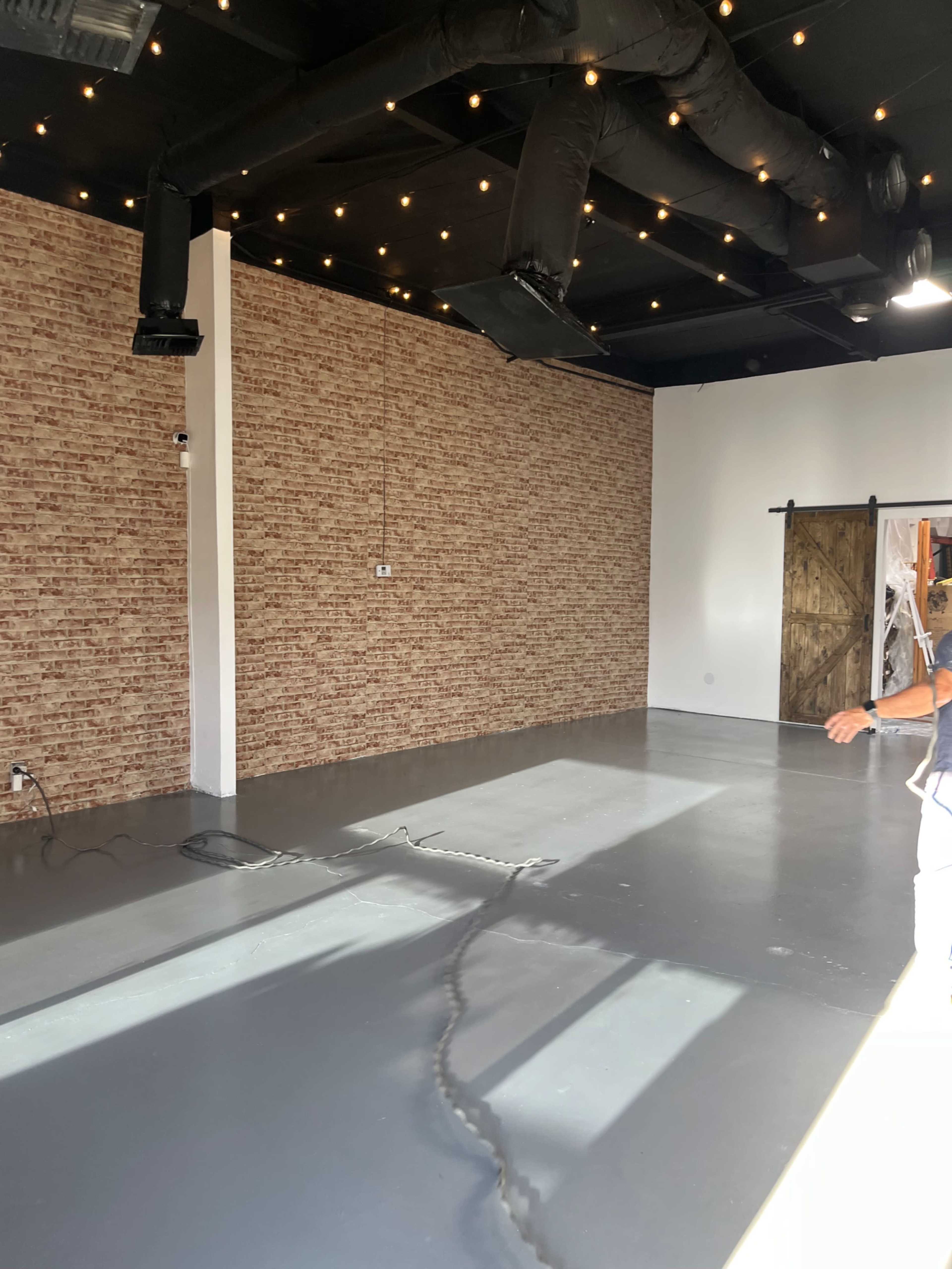 The image shows an empty room with a brick-patterned wall, polished gray flooring, and exposed ceiling ducts.