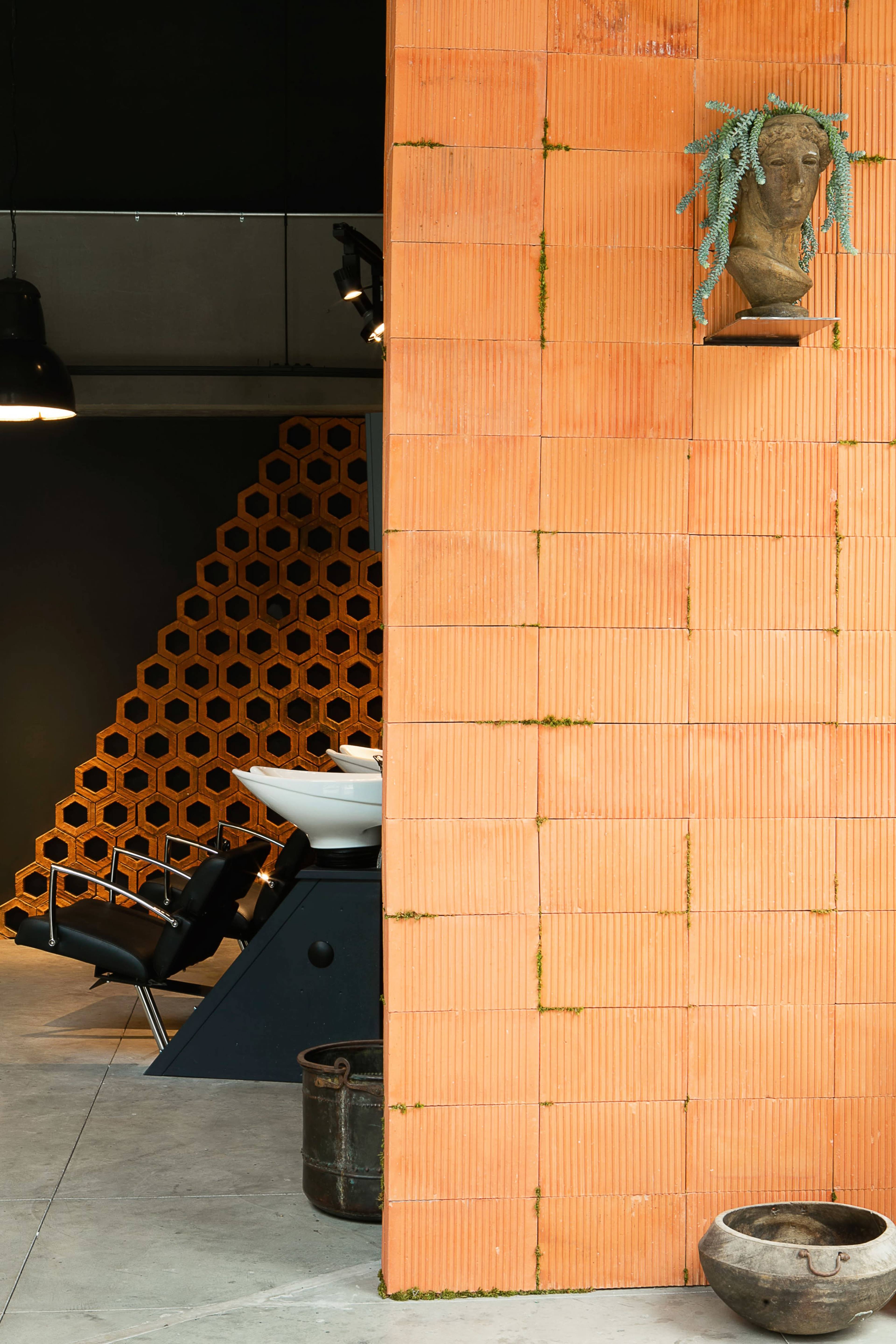 An interior space featuring an orange textured wall, a black styling station with a chair, and decorative elements such as a sculpture and various containers.