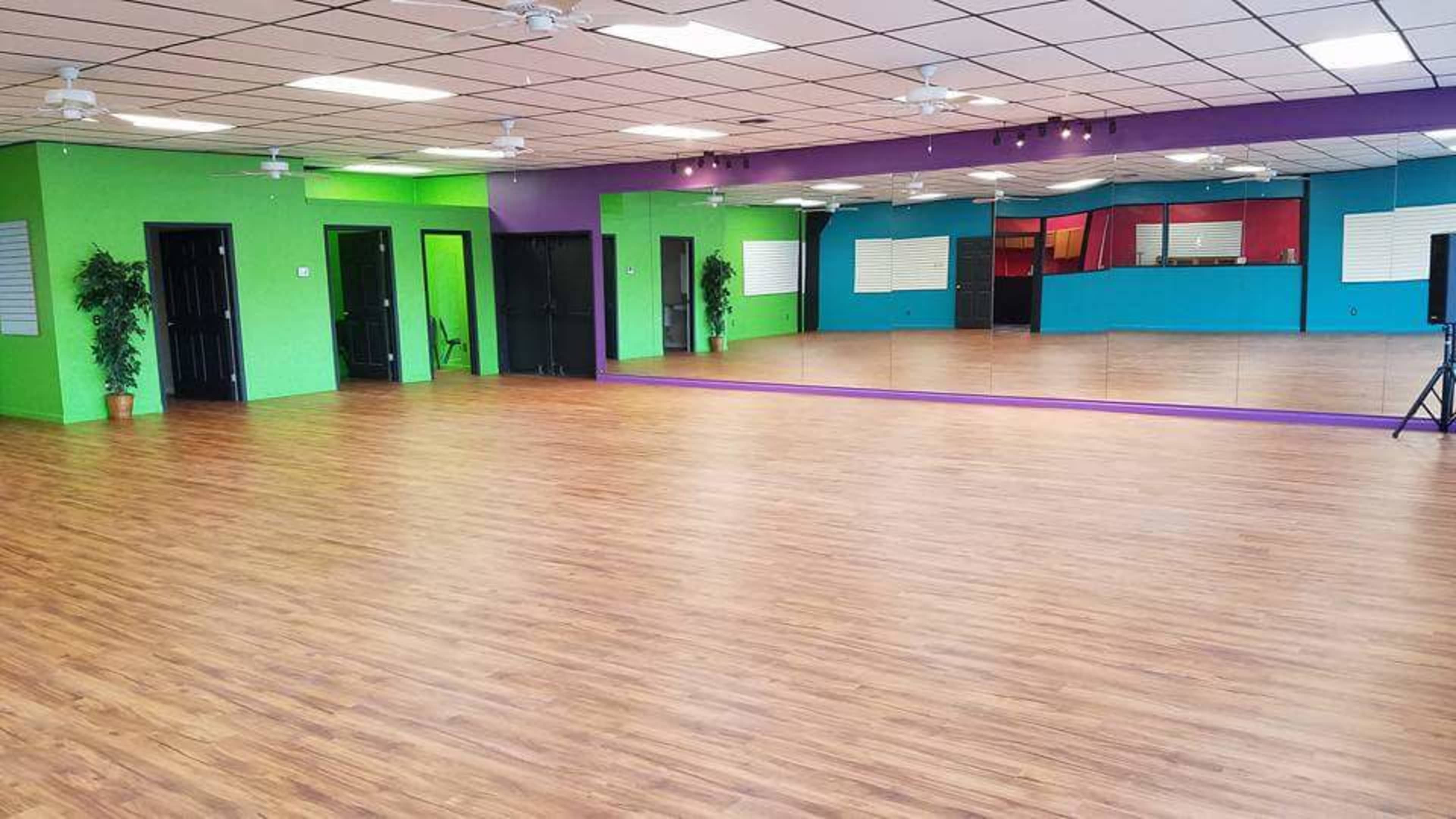 A spacious dance studio featuring wooden floors, mirrors on one wall, and brightly colored painted walls.