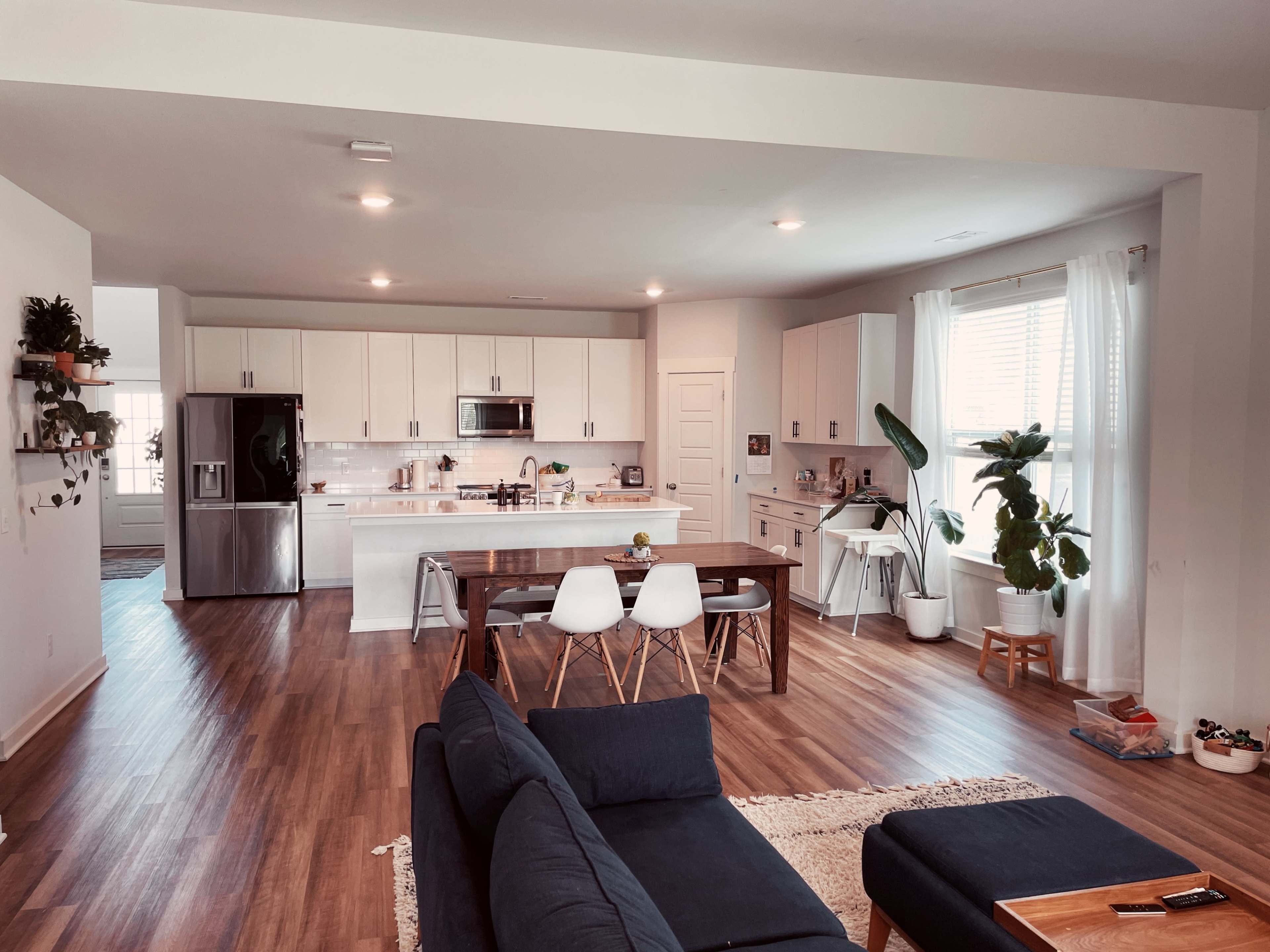 A modern kitchen and dining area features a wooden table, chairs, and a spacious layout with appliances and plants.