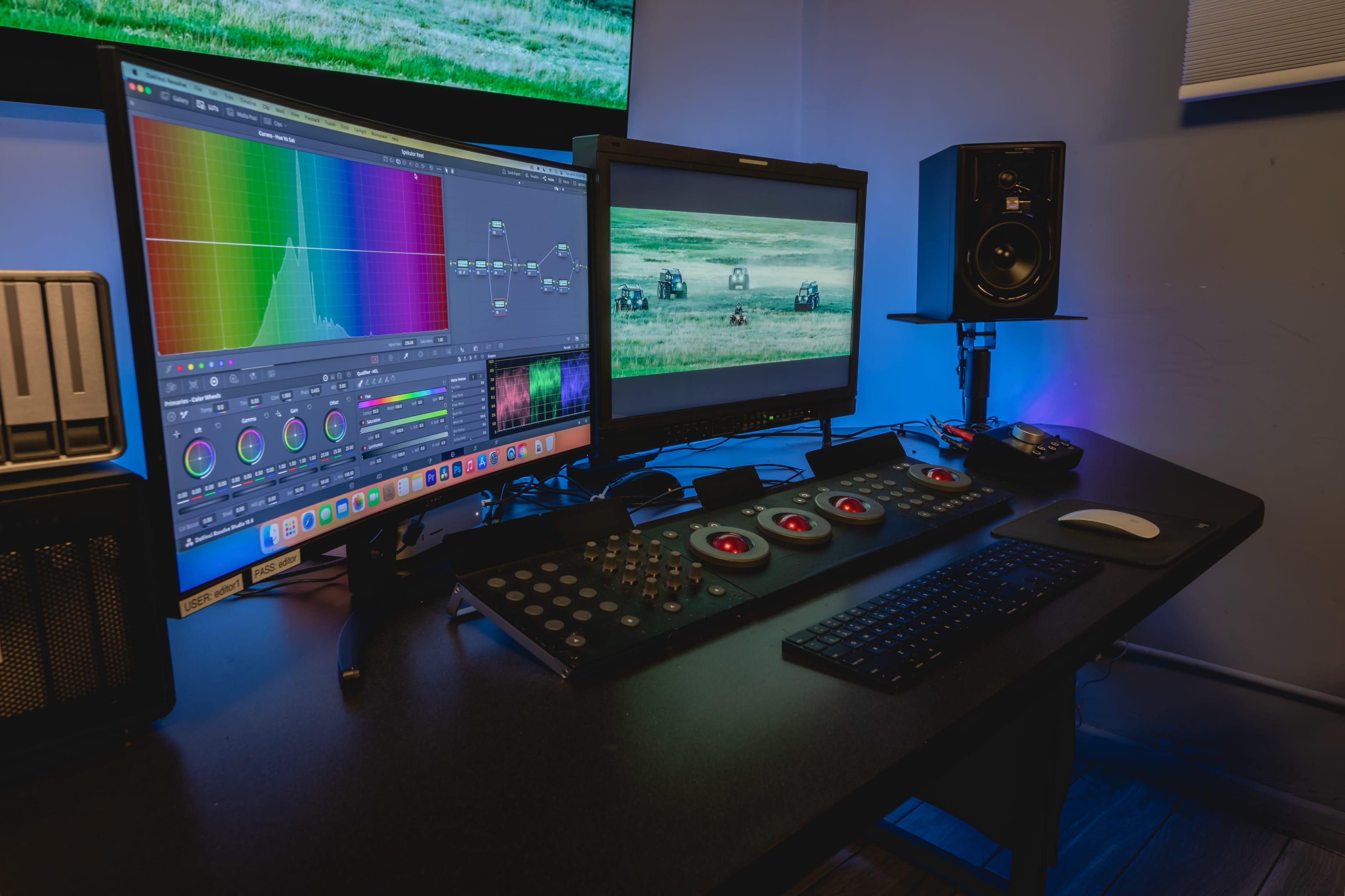 A video editing workstation features two monitors displaying color grading software, a film scene, and a control panel with buttons and a keyboard.