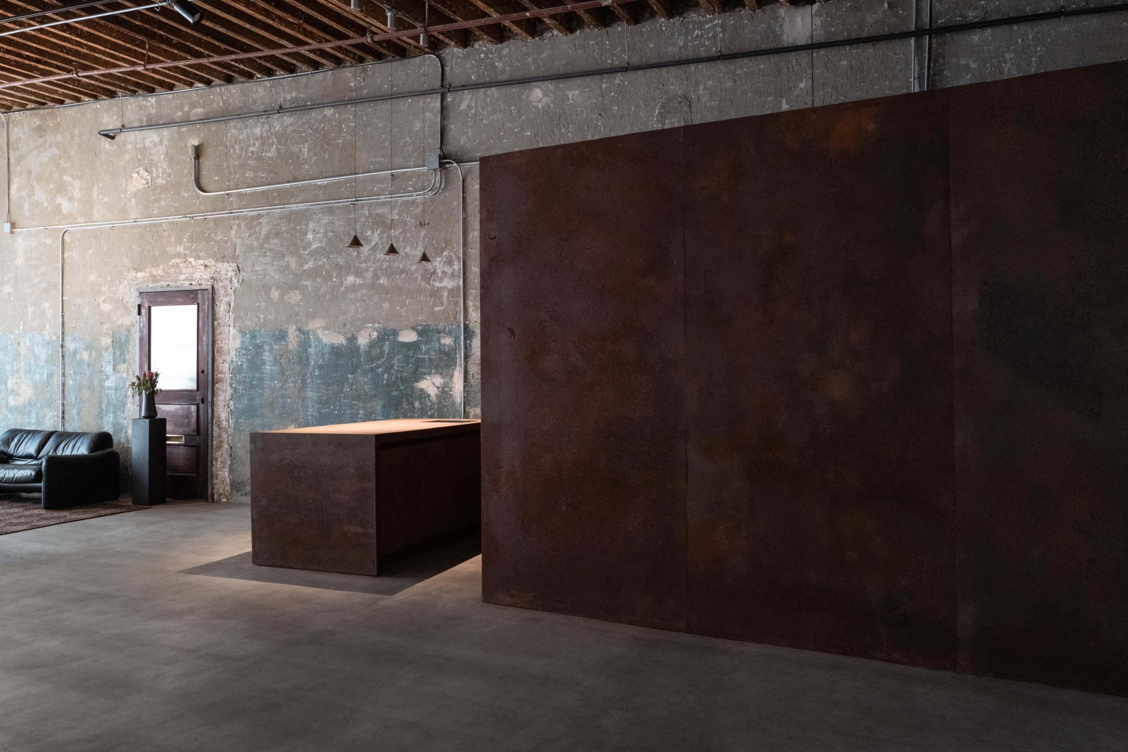 The image shows a spacious interior featuring a rust-colored reception desk and a textured wall, with a doorway in the background leading to another room.