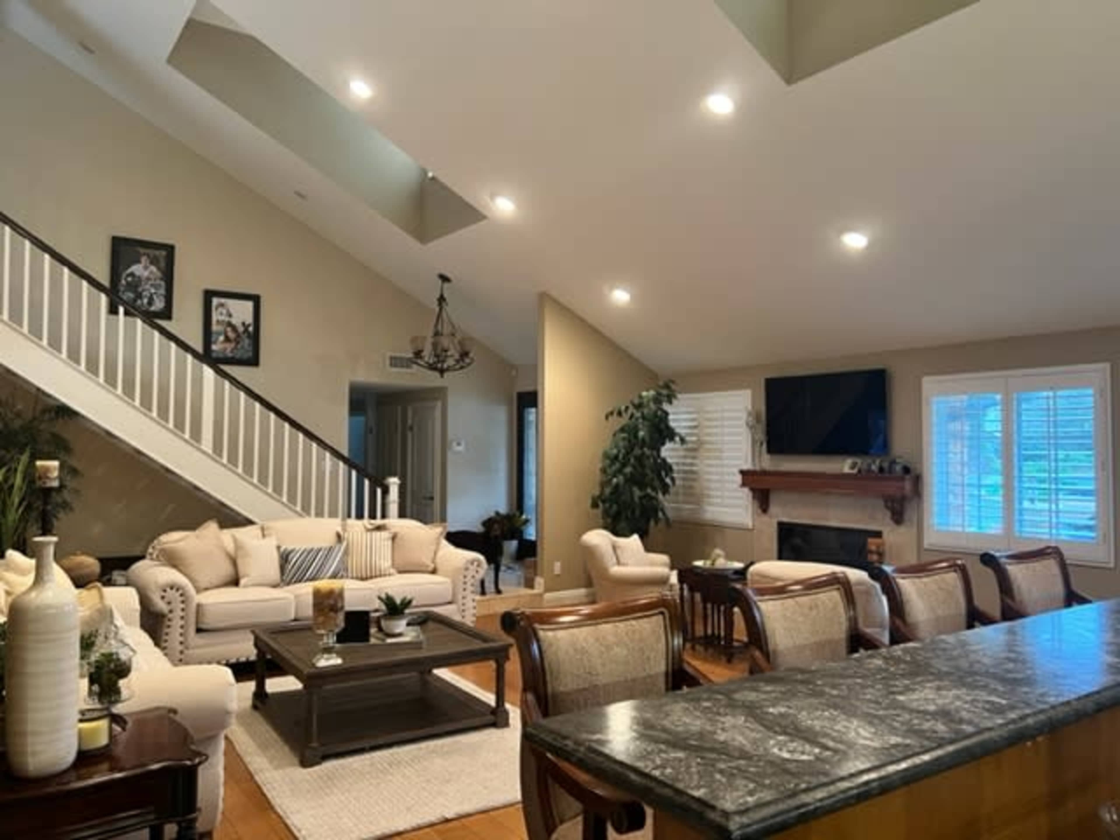 A spacious living room with a beige sofa set, a wooden coffee table, and a staircase leading to an upper level, complemented by large windows and a fireplace.