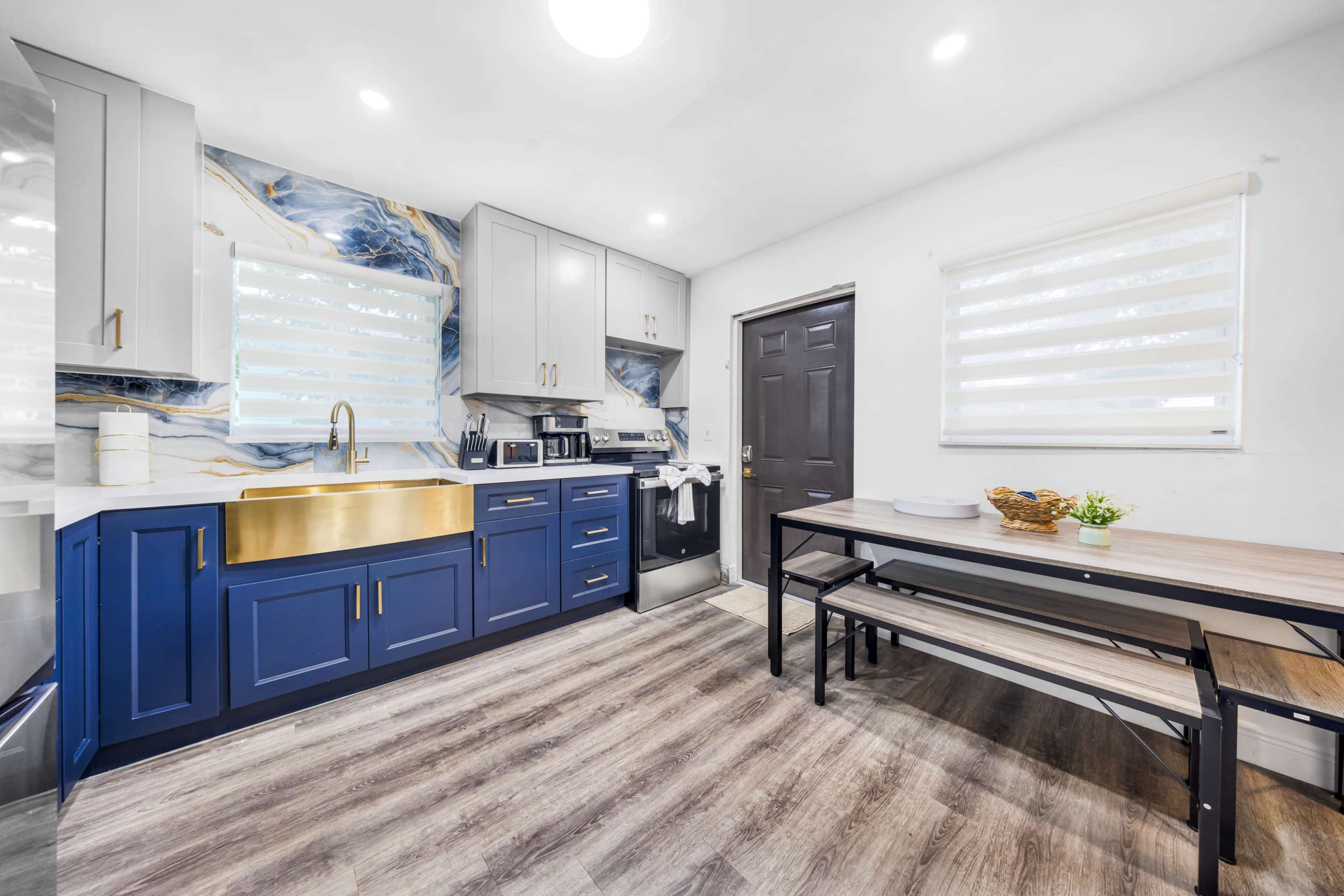 The image shows a modern kitchen with navy blue cabinets, a gold sink, and a wooden dining table.