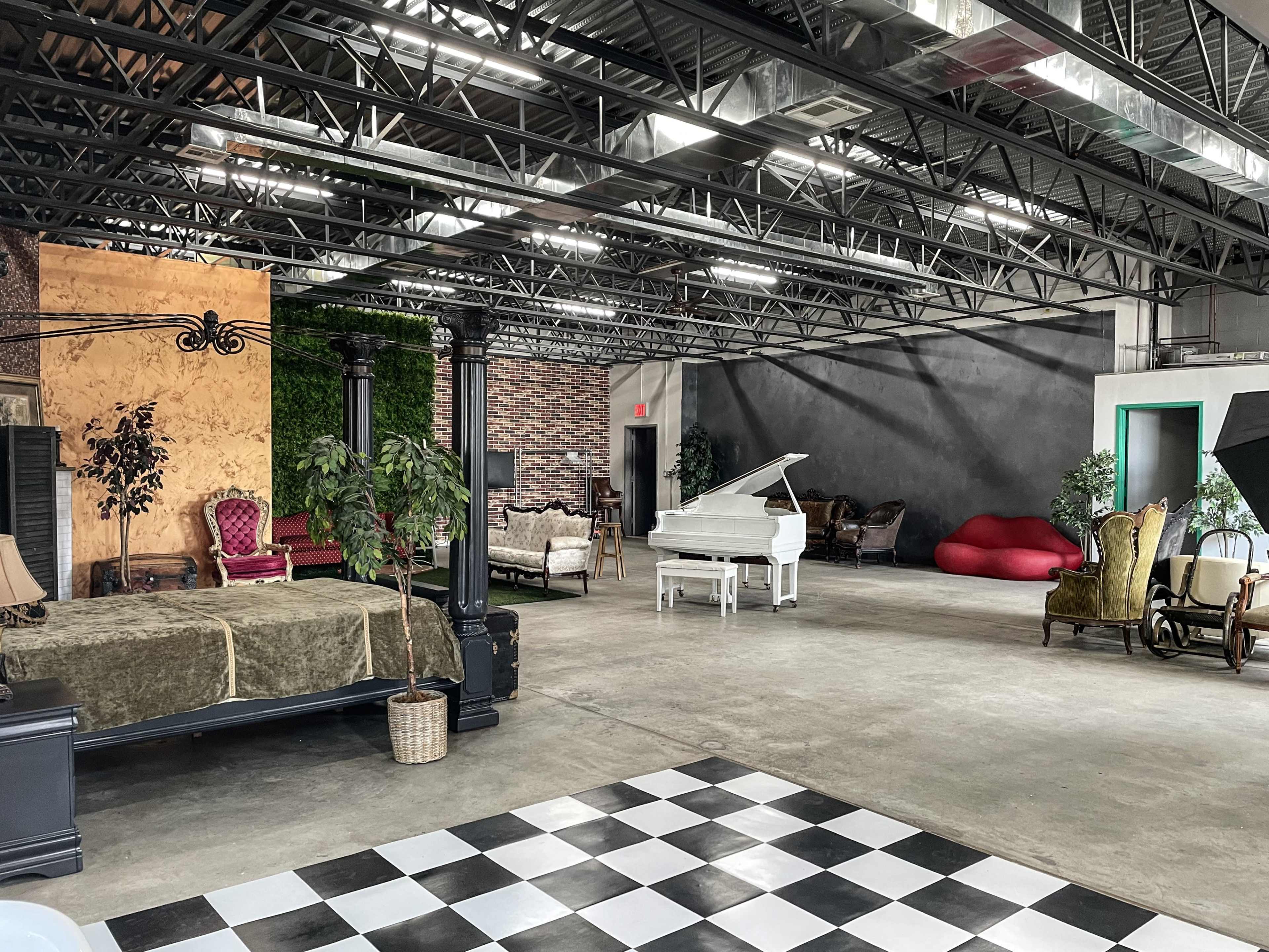 A spacious studio with various seating arrangements, including a grand piano, a bed, and decorative furniture against textured walls.