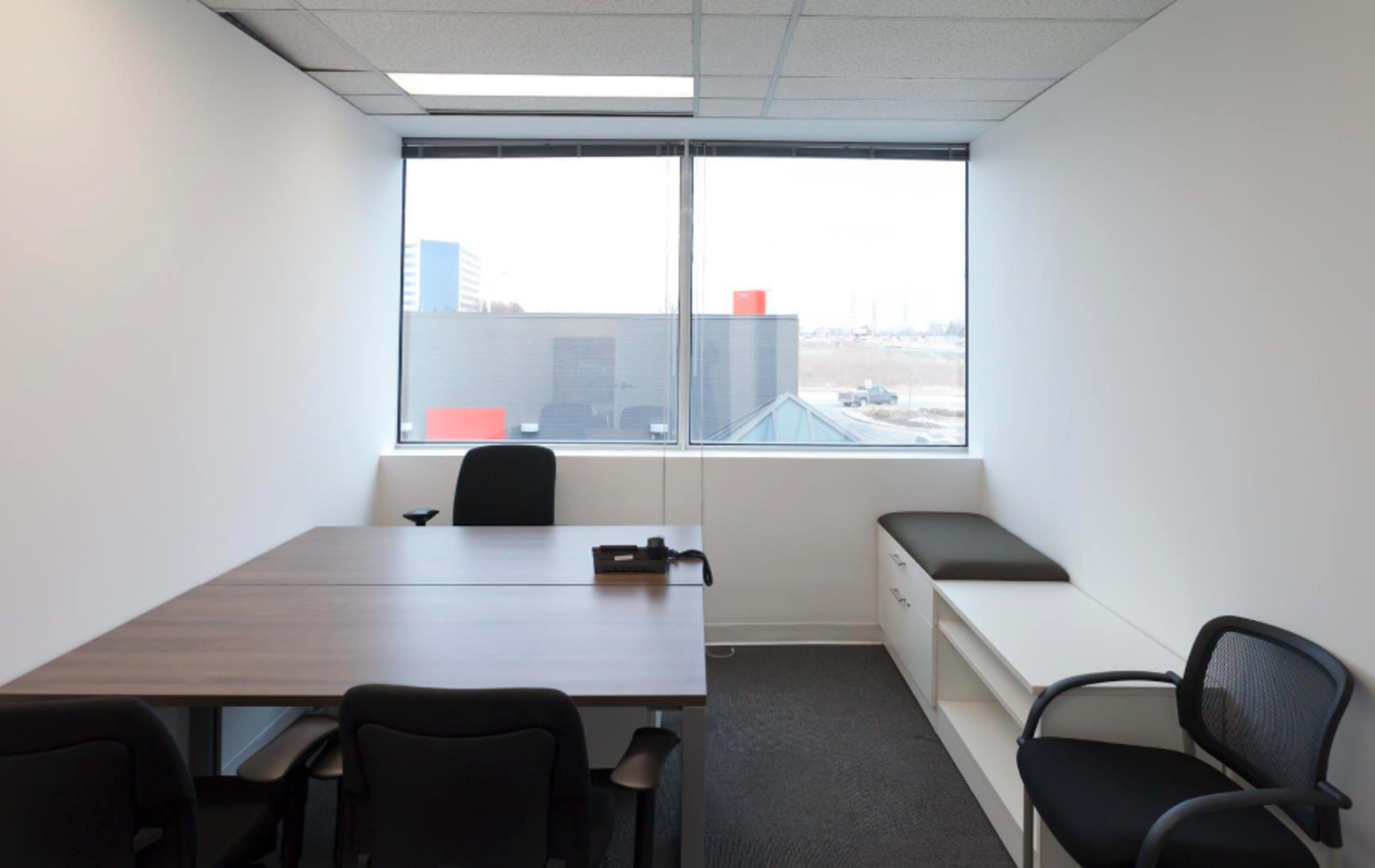 A small office with a table, four chairs, and a window showing an urban view.