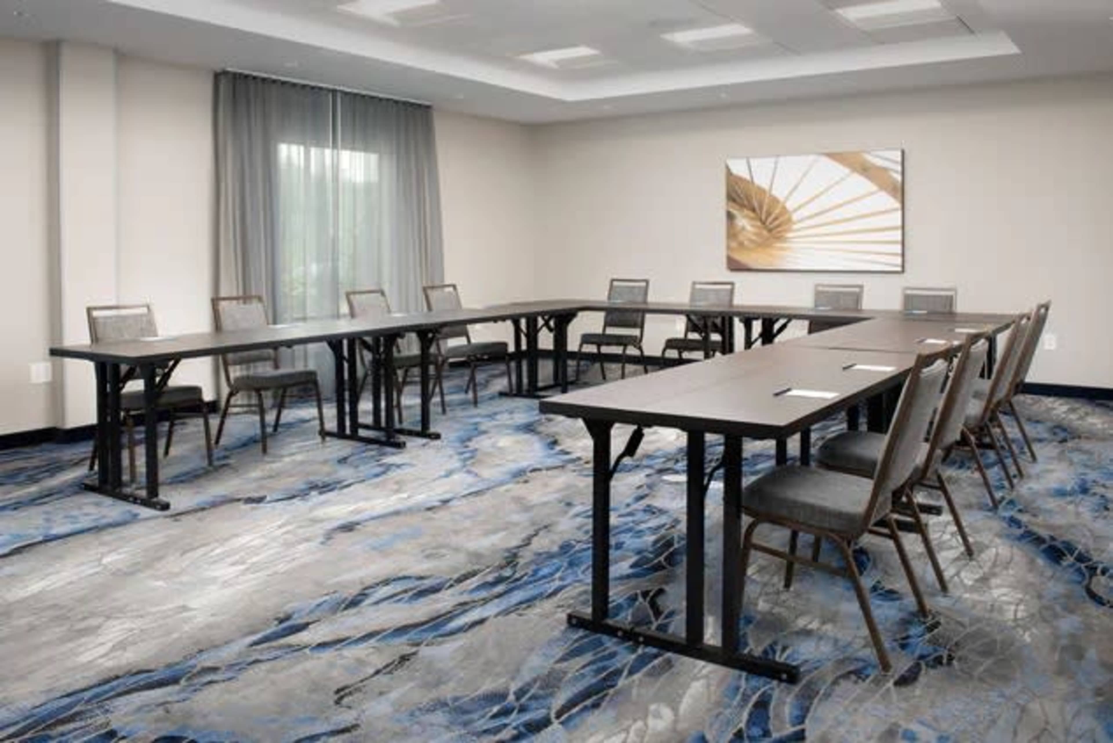 The image shows a modern conference room arranged with several rectangular tables and chairs on a patterned carpet.