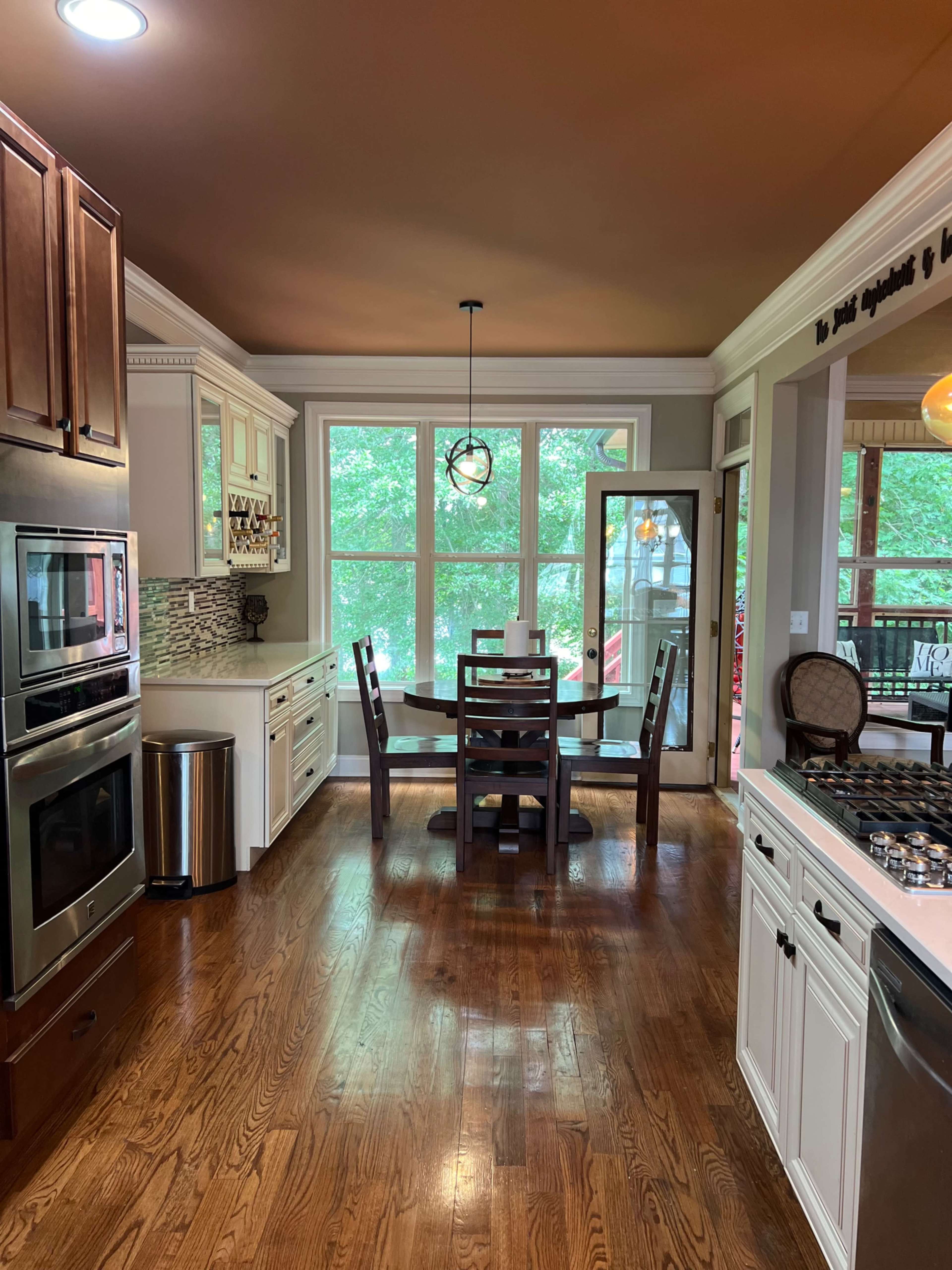 A modern kitchen with wooden cabinets and a dining area featuring a table and chairs beside large windows overlooking a deck.
