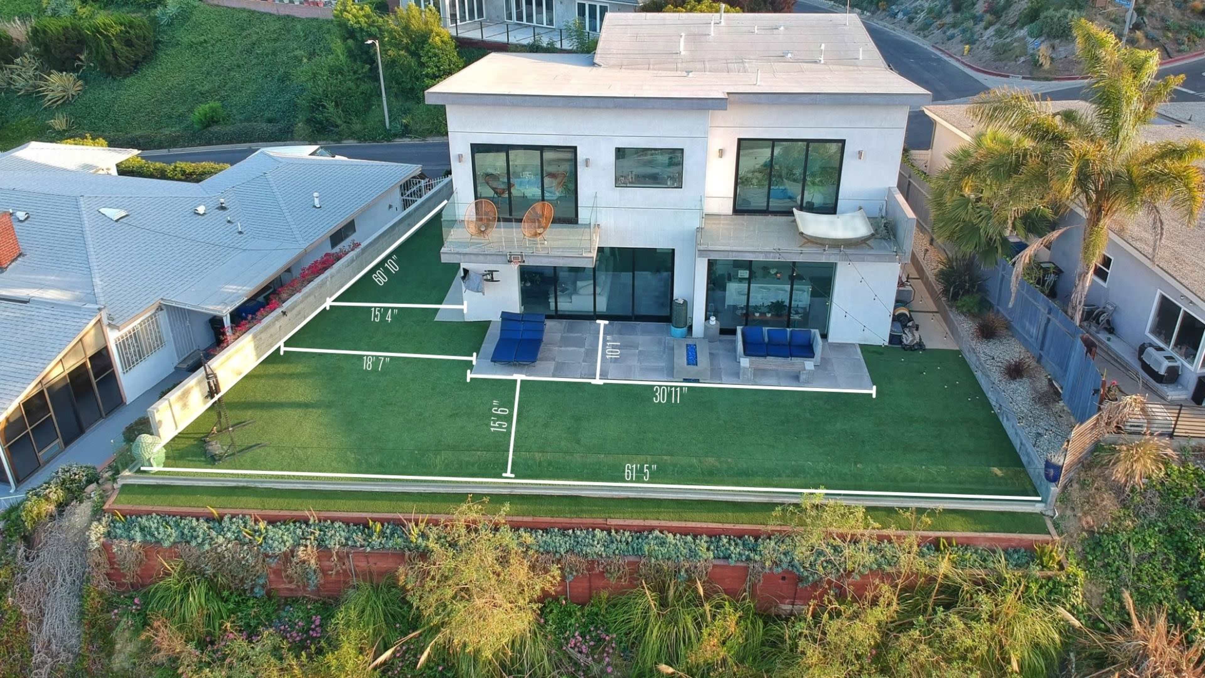 A modern house with large windows and a lawn marked with yard lines for measurements, situated on a hillside.