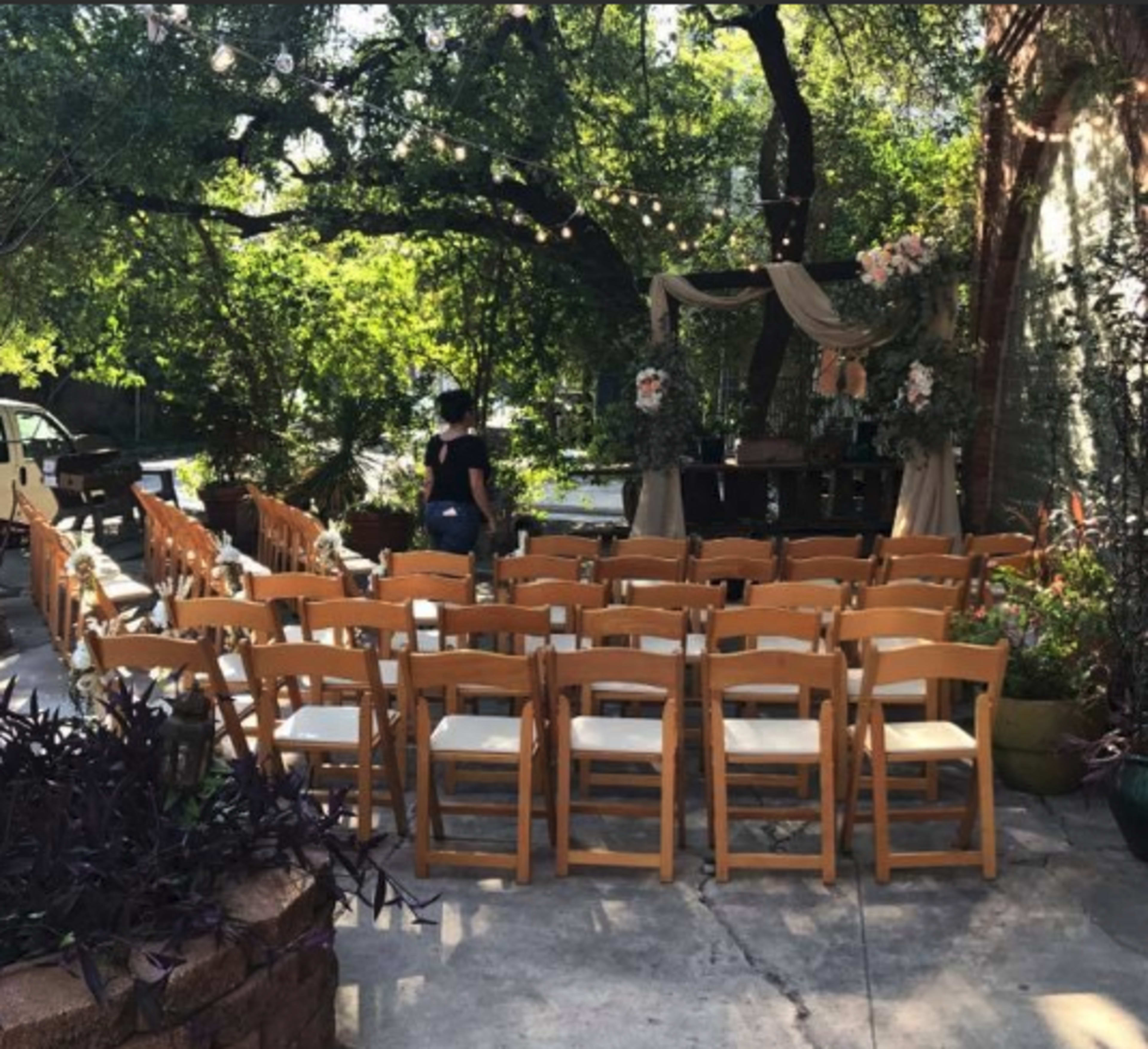 A set of wooden chairs arranged in rows in an outdoor setting decorated with floral arrangements and draped fabric.