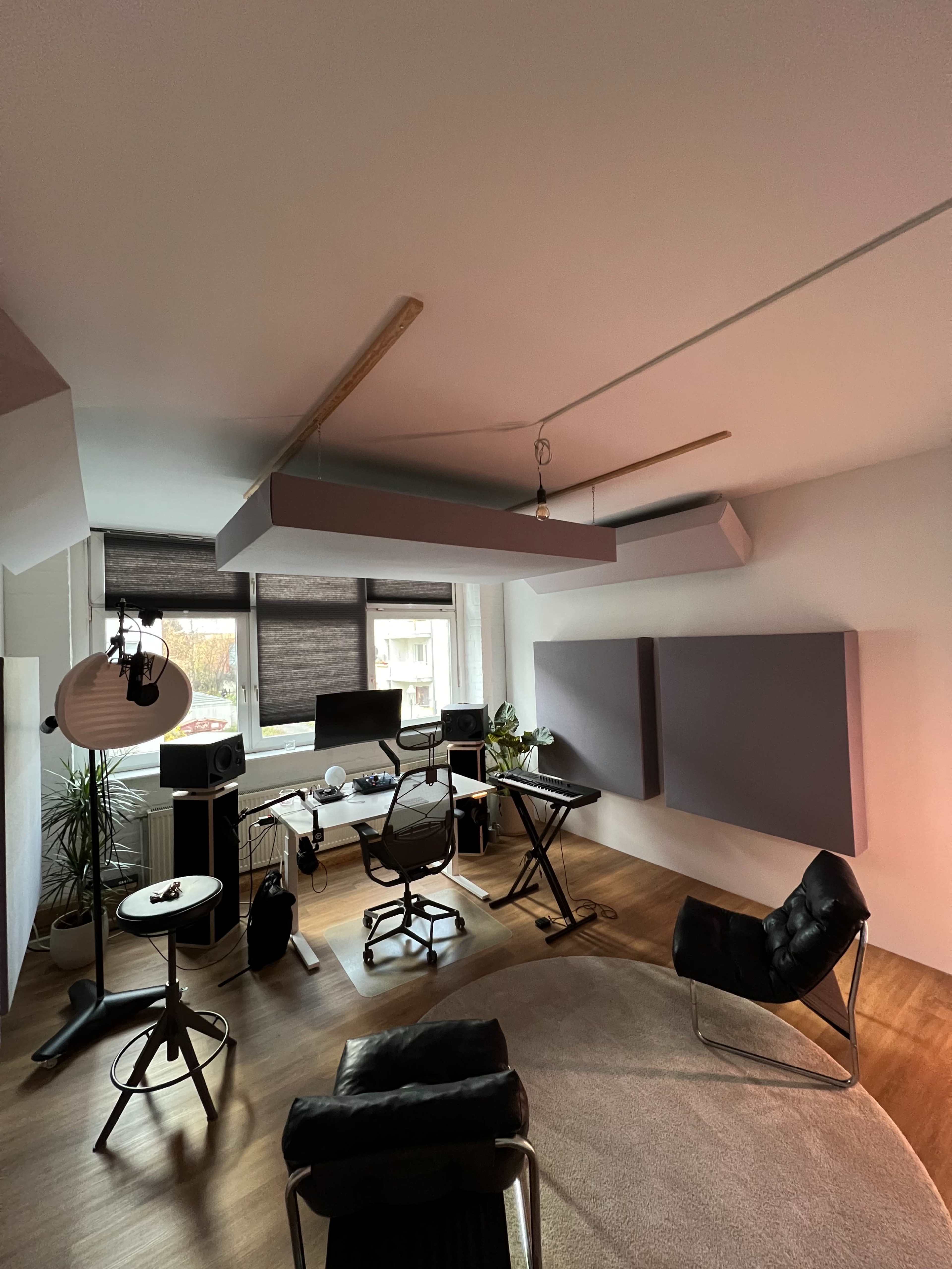 The image depicts a modern home office featuring a desk with computer equipment, a black office chair, and soundproof panels mounted on the walls.