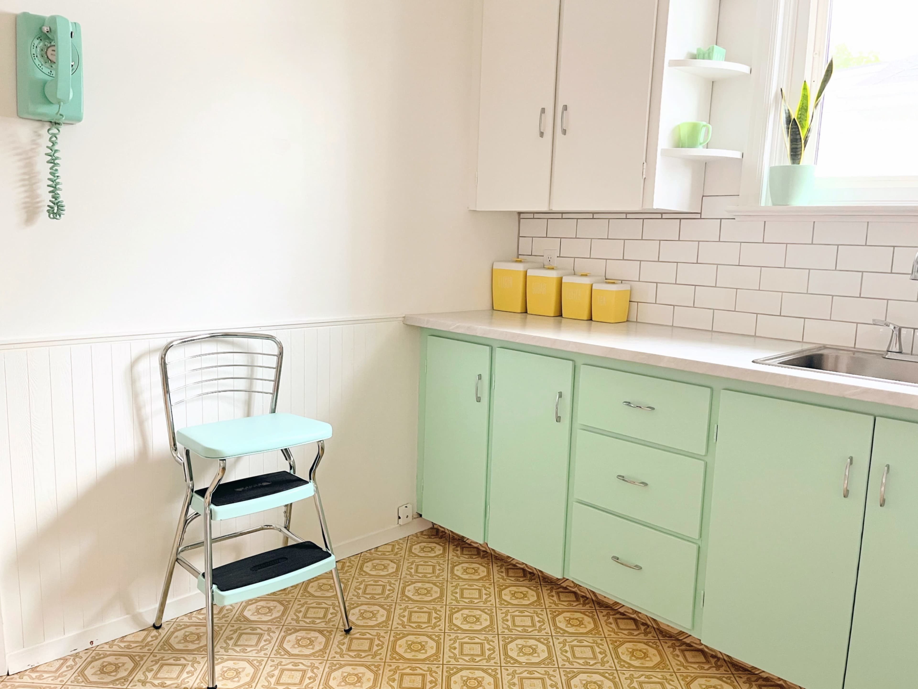 A light mint green kitchen with a metal step stool, white cabinets, and yellow containers on the countertop.
