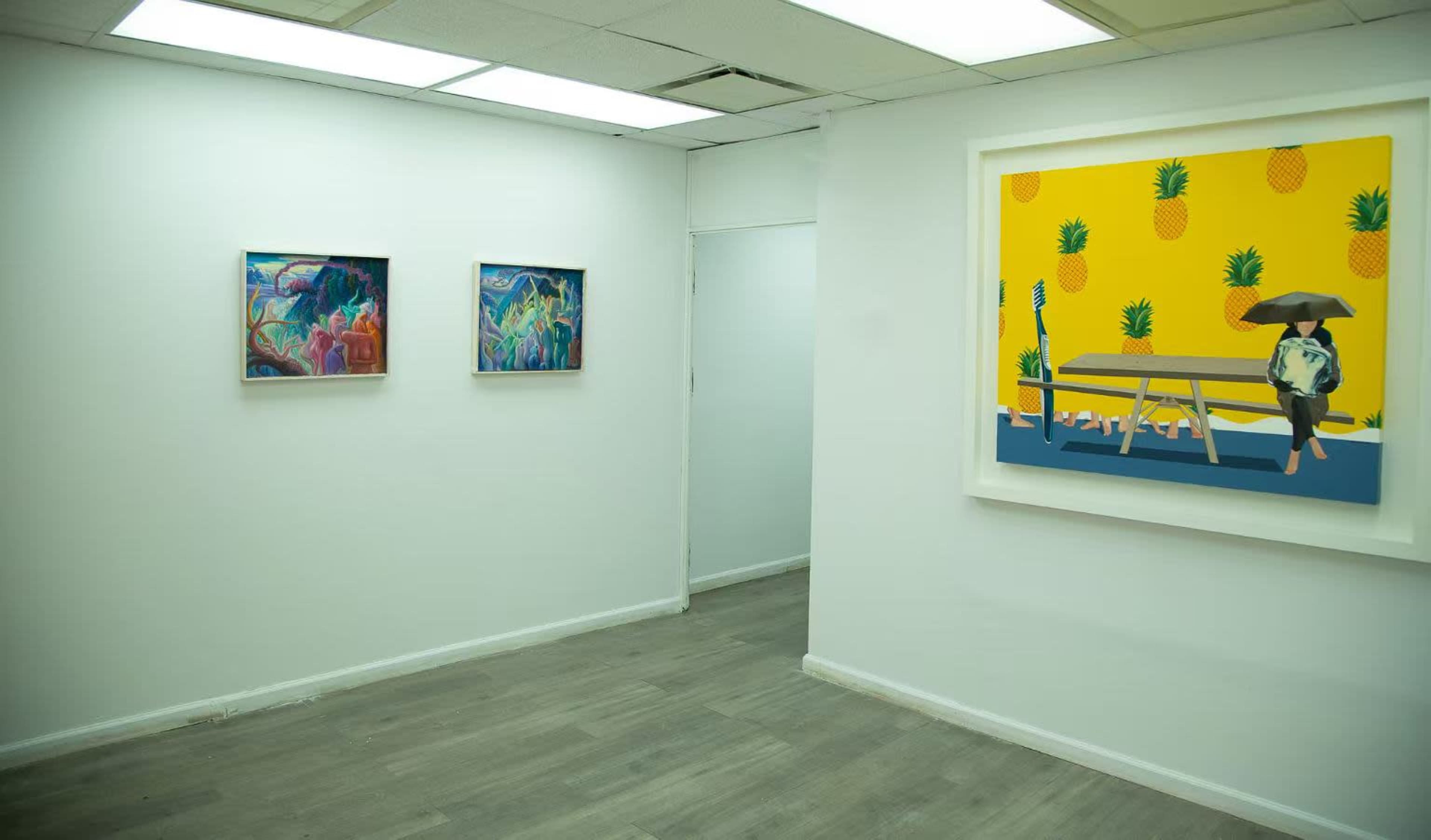 The image shows a brightly lit gallery space with two colorful paintings on the left wall and a large, vibrant artwork featuring a figure under an umbrella on the right wall.