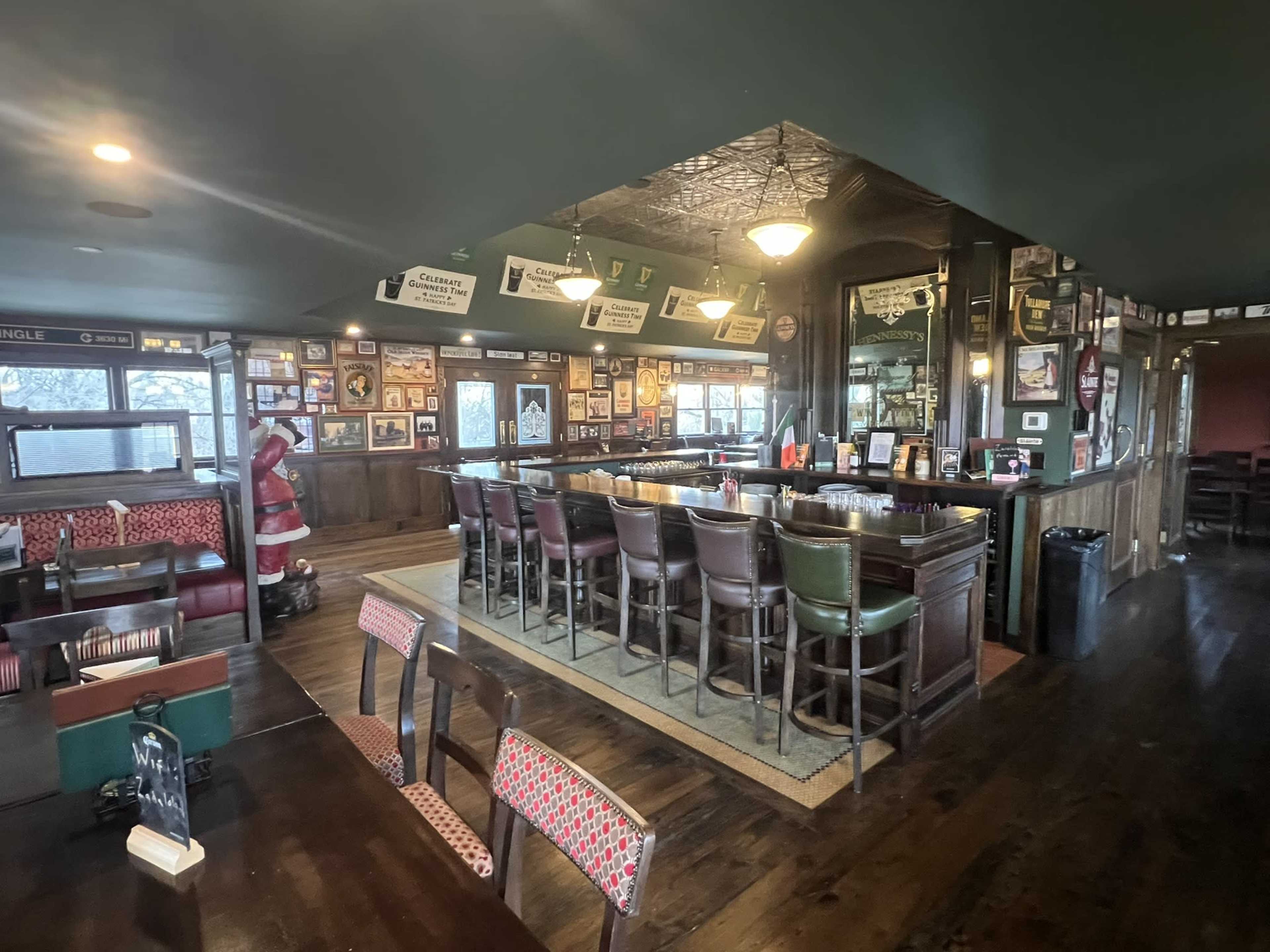 The image shows the interior of a pub with wooden flooring, a bar area lined with stools, and framed photographs on the walls.